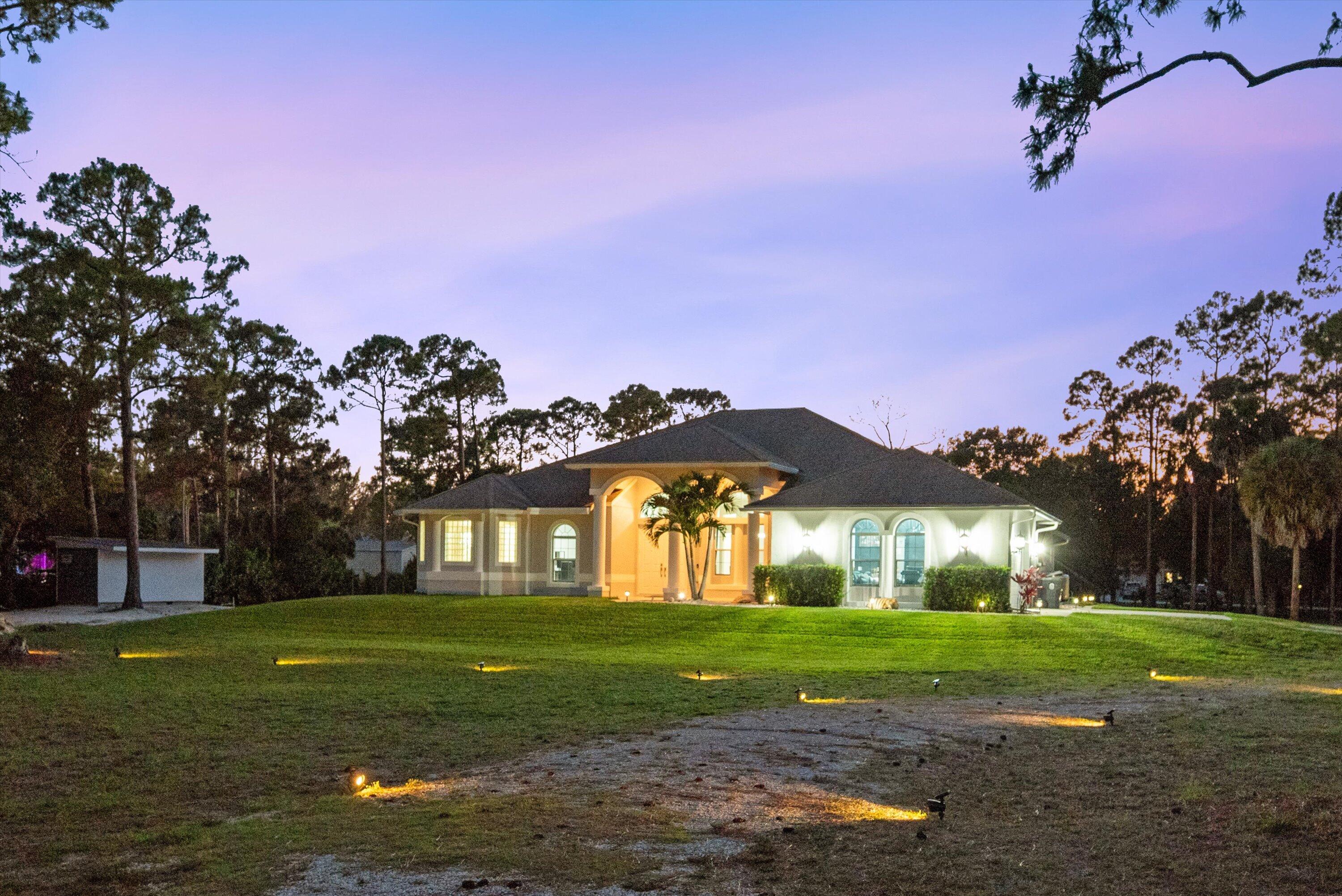 A private waterfront sanctuary on 2.5+ acres in the heart of Loxahatchee's premier equestrian corridor, this custom estate delivers an extraordinary blend of luxury, privacy, and refined country living rarely found at this price point. Set on expansive acreage with approximately 260 feet of tranquil waterfrontage, this exceptional residence offers over 4,100 square feet of sophisticated living space, including 5 bedrooms, 4 bathrooms, dedicated office space in both the main residence and detached guest residence, and two full kitchens designed to accommodate multigenerational living, private guest accommodations, executive workspace, or extended entertaining.  Designed to impress both indoors and out, the estate features expansive entertaining spaces, premium upgrades throughout, and seamless indoor-outdoor living framed by sweeping water views and lush tropical surroundings. Every detail of the property reflects pride of ownership, quality craftsmanship, and thoughtful investment into both aesthetics and long-term functionality. The sprawling acreage provides endless flexibility for equestrian use, additional structures, RV or boat storage, private recreation, or future customization — all while maintaining the exclusivity and elegance expected of a premier Palm Beach County estate. Located on a paved road within one of South Florida's most desirable acreage communities, this property offers the perfect balance of secluded luxury living with convenient access to Wellington's world-renowned equestrian venues, upscale dining, shopping, airports, and coastal amenities. An exceptional opportunity for luxury buyers seeking a turnkey estate property with land, waterfrontage, privacy, and uncompromising value
