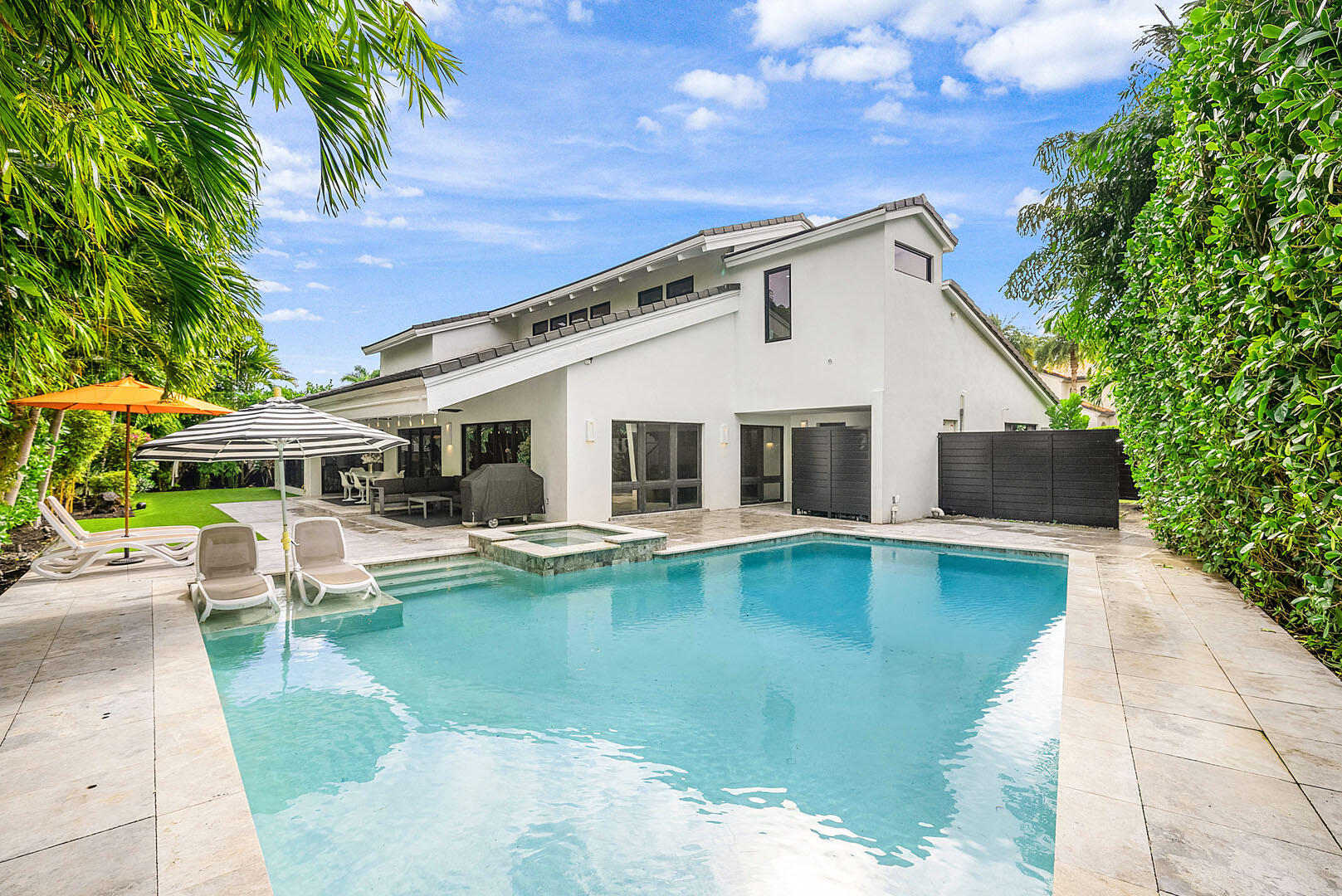 A refreshed two-story mid-century modern residence, this home is defined by dramatic vaulted wood ceilings, warm architectural character, and an effortless sense of style across just over 4,000 square feet of living space. Designed for both everyday comfort and elevated entertaining, the layout offers four spacious bedrooms and four-and-a-half beautifully appointed baths. At the heart of the home, a gourmet eat-in kitchen features a striking center island and premium appliances, creating a natural gathering place for family and guests alike. A glass-enclosed study overlooks the shimmering pool, offering a serene workspace framed by views of the backyard oasis. Step outside to a private retreat where a custom heated pool and spa invite year-round enjoyment, complemented by an outdoor shower and low-maintenance turf landscaping. The covered patio is perfectly arranged for al fresco dining and relaxed lounge seating, delivering the ideal indoor-outdoor lifestyle. The primary suite is a true sanctuary, complete with a spa-inspired bath and dual walk-in closets. Additional highlights include natural gas service, a generator, and impact glass throughout providing comfort, security, and peace of mind in a residence that feels both timeless and perfectly updated.