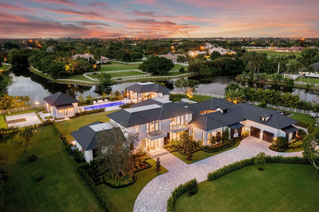Mi Tierra Delray Beach is an impeccable new contemporary estate offering rich organic design set on nearly 3 acres of idyllic lakefront property. This custom multidimensional compound is situated behind private gates of Tierra Del Rey, an exclusive and sought-after community in Palm Beach County. 
 
The waterfront estate consists of three distinct structures offering the utmost in privacy and modern family lifestyle. It encompasses 10,099 square feet of living space and 12,973 square feet in total. The property features finest materials, craftsmanship and sophisticated organic design and neutral hues. The property features 6 bedrooms, 7 baths, 2 half baths, including main level owner's site with dual baths and closets. An exquisite double-island kitchen and adjacent living area, cast predominantly in brilliant white with light hardwood flooring and similarly toned wood-beam ceiling insets, sets a comfortable chic aesthetic thread that runs throughout many of the rooms. In the case of the chef's kitchen, charcoal cabinetry around the double islands and cooking area (which includes state-of-.the-art appliances) provides a striking contrast to the impressive white silestone quartz countertops. 
 
The open layout possesses an indoor-outdoor flow that seamlessly integrates yet another outdoor entertainment area. This one with a gas fireplace built into a white-brick designer wall that feels like an extension of the family room. Other interior highlights include a media club room with a full wet bar; a cozy theater room; a lush courtyard with a stone firepit, an upstairs den; laundry rooms on first and second floors, and a mammoth playroom. The home is equipped with Crestron Home Automation providing control of audio, video, climate and security.
 
A stone pathway from the lakefront dock leads to a custom-designed pool area bookended by a separate guest house and fitness facility. The one-bedroom, one-bathroom guest house is a sanctuary unto itself. It is complete with a full bedroom, bath, kitchen area, family room and separate waterfront private patio. The rustic outdoor entertainment area is bathed in warm woods, with a summer kitchen, counter seating, a flat-screen TV, and a stone dining table. 
 
The sprawling two-floor main house extends the clean-lined modern aesthetic with country chic accents. Exterior extras, meanwhile, abound. Along with a turf bocce court, a half basketball court made from custom versa-court tiles, the lushly landscaped property provides a variety of outdoor perches (including a terrace off the master bedroom and seating under a row of banyan and fruit trees), 16 x 54 Pool with underwater speakers, a garden area and a fully functional chicken coop.
 
Experience Mi Tierra Delray Beach.