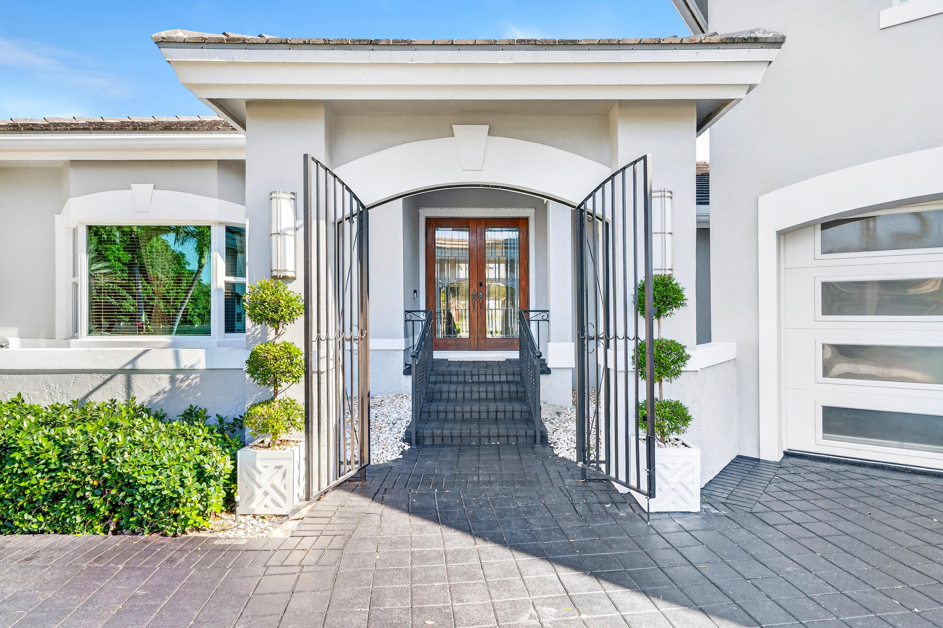 Bring your cherished collectible cars to this spectacular contemporary residence, perfectly tucked away on a peaceful cul-de-sac overlooking the fresh waters of Lake Mangonia. Custom built in 2019 by the current owner, this gracious home offers a versatile canvas designed to complement a wide range of taste and lifestyles. Nestled in the heart of West Palm Beach within the prestigious gated community of Presidential Estates, the property features a luxurious first-floor primary suite with a spa-inspired en-suite bath, a private workout/massage room, and a flexible loft space ready to adapt to your needs. Soaring ceiling and expansive windows bathe the interiors of this home in natural light, creating an open, airy atmosphere. Multiple pocket, sliding glass doors seamlessly connect the living space to the pool and terrace, inviting year-round enjoyment of Florida's indoor-outdoor lifestyle. The spacious backyard framed by endless lake views, sets the stage for unforgettable entertaining, alfresco under the stars, relaxed lounging, and of course, productive work-from-home days. Above the 3-car garage with 3 lifts for 3 additional cars, is a beautifully appointed one-bedroom apartment with a kitchen that provides the perfect retreat for guests/family/au pair. This home is more than a residence - it's a lifestyle, offering elegance, comfort, and endless possibilities in one of West Palm Beach's most desirable communities.