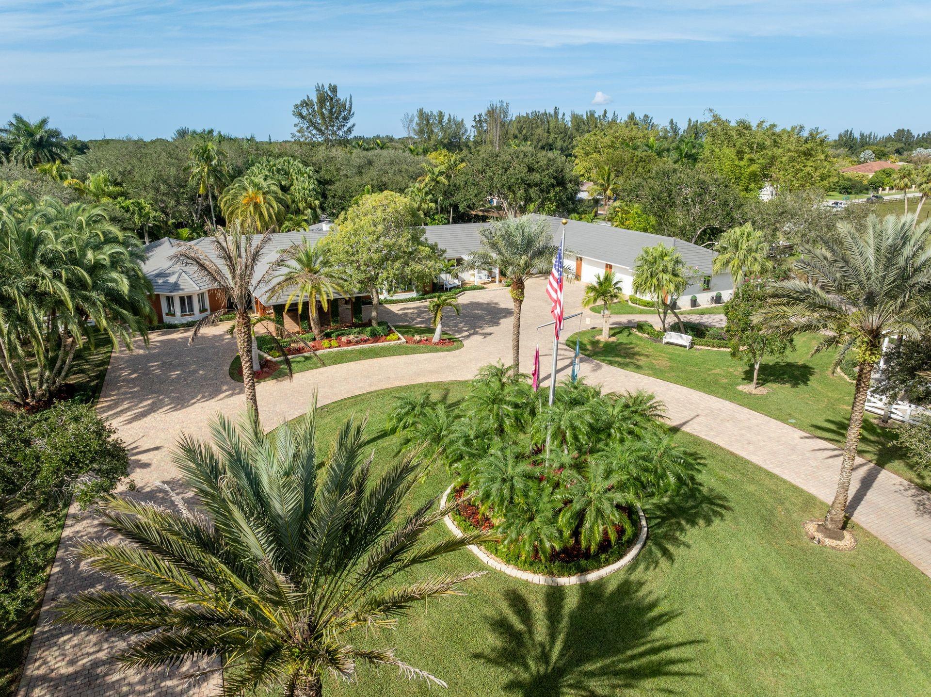 Nestled on 5 private acres, this extraordinary estate spans 10,000 SF and offers a world-class lifestyle with a full equestrian center, separate guest home, private sauna, and lush gardens featuring a gazebo and koi pond. Ideally located just 30 minutes from Miami and Fort Lauderdale airports, this hidden oasis combines luxury, security, and resort-style living. Behind grand gates, the main residence is designed for both lavish entertaining and everyday comfort, showcasing 5 bedrooms, 4.5 bathrooms, a home theater, billiards room, office, and gym. Brazilian hardwood floors, coffered ceilings, and a chef’s kitchen with marble finishes elevate the sophisticated interiors. The primary suite and newly renovated spa-like bathroom opens to a serene outdoor retreat. Beyond the billiards room and theater, an oversized guest suite and private gym offer added flexibility. Three additional bedrooms occupy a separate wing, including a second primary bedroom and two more that share a Jack-and-Jill bath. The grounds are equally impressive, featuring a professional equestrian center and riding arena, a resort-style saltwater lagoon pool with waterfalls, 2,500 sq. ft. of detached office space, and a separate guest house. A 12-person sauna, fishing pier, and private lakeshores complete the serene setting. A five-car garage provides ample parking, while a 16-camera security system offers peace of mind. With unparalleled privacy and natural beauty, this estate feels like living inside your own private national park.