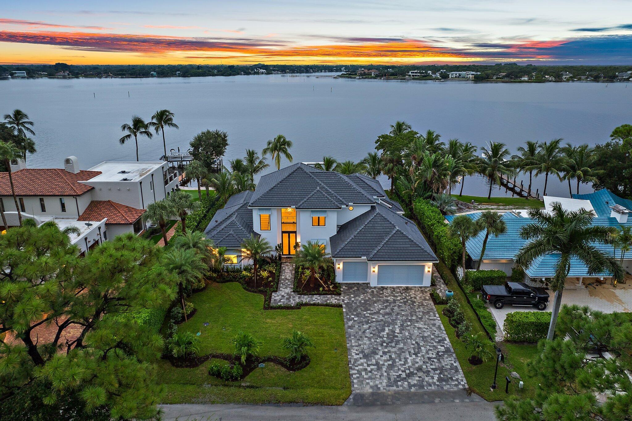 Introducing an elegant Bermuda-style custom residence, perfectly nestled in the charming Bay Harbor neighborhood, a serene enclave of just 15 homes with only 9 being located on the waterfront within the quaint Village of Tequesta. This exquisite 5-bedroom, 6-bath home boasts over 100 feet of frontage on the scenic, historic Loxahatchee River, offering breathtaking wide-water views from every room. As you approach, an elegant paver driveway and walkway guide you to a fabulous 2-story glassed entryway, bathing the home in natural light.  In the main living area, you will find more spectacular views and a stunning wet bar for the entertainer.  Adjoining the family room, a spectacular chef's kitchen is equipped with top-of-the-line appliances and Downsview Cabinetry, perfect for culinary enthusiasts, who will appreciate the panoramic views across the pool area and plush backyard. An oversized first-floor master bedroom suite overlooks the backyard and wide-water views, providing dramatic daily sunrise and sunset scenes.  All 4 upstairs bedrooms are ensuite, each with its own walk-in closet complete with custom cabinetry, and a bathroom with stunning designer finishes.  A spacious mud room and laundry room with cabinets galore are conveniently located adjacent to the kitchen and near the 3-car air-conditioned garage, also complete with custom cabinetry, which is sure to impress the car collector. The lushly landscaped grounds feature a heated resort-style pool and spa, a sitting area ready for a gas fire pit, and an artificial turf inlay ideal for relaxation and entertaining.  With a new seawall and dock, this property provides easy access to the water, making it just a 5-minute boat ride to the Jupiter Inlet and the Atlantic Ocean. Enjoy panoramic sunset views over the widest part of the Loxahatchee River from this extraordinary home.