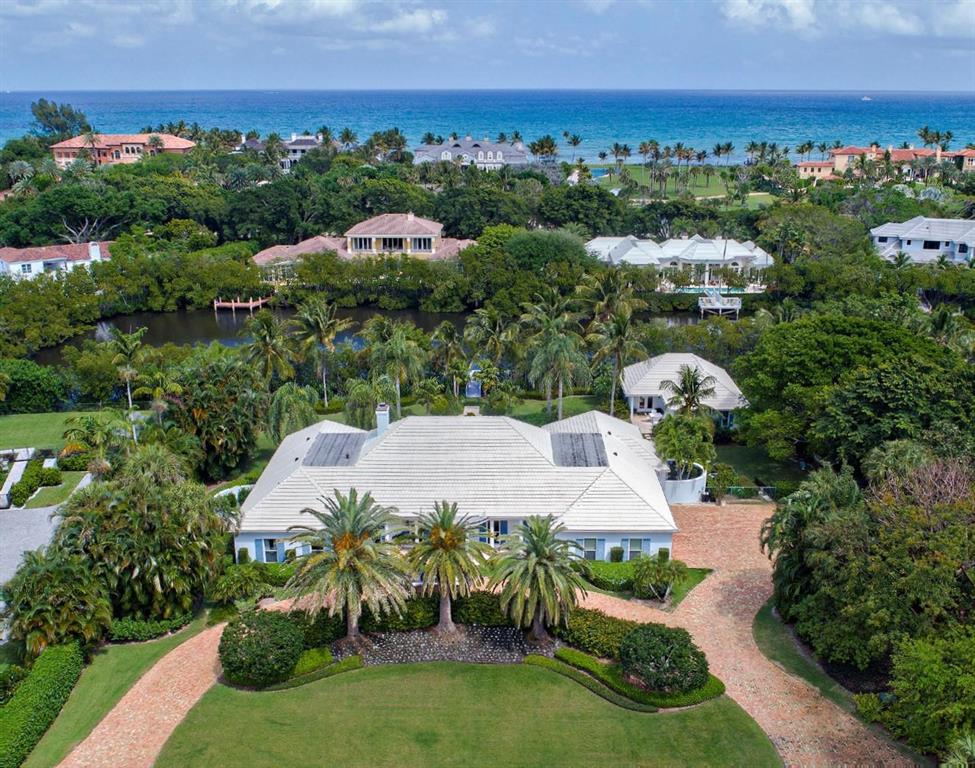 This beautiful pale blue island colonial is in prestigious Seminole Landing in North Palm Beach.  Stately columns highlight the covered entry off the circular brick paved drive.  As you enter, the foyer is flanked on the left by the family room featuring exquisite pecky cypress paneling, molding details and custom millwork.  To the left is the large formal dining room with an ornate parquet wood floor. The expansive living room is perfect for entertaining with its wet bar and fireplace, and high pecky cypress tray ceiling.  Glass doors open to the outdoor covered patio and the lovely pool area. The split floorplan has four guest bedrooms, a den, and a wood paneled office on the left side of the home, and the kitchen, informal dining, and large master suite to the right. To the rear of the property amongst the lush tropical landscaping sits a secluded one-bedroom guest house highlighted by its large entertaining area, wet bar and built-in outdoor BBQ. The home sits on 1.1 acres and is 7,714 total square feet with 6,135 under air (Main House 4,867, Guest House 1,268).  It has a three-car garage, and a dock.  The property is a short ride to one of the most beautiful private beaches in the area.