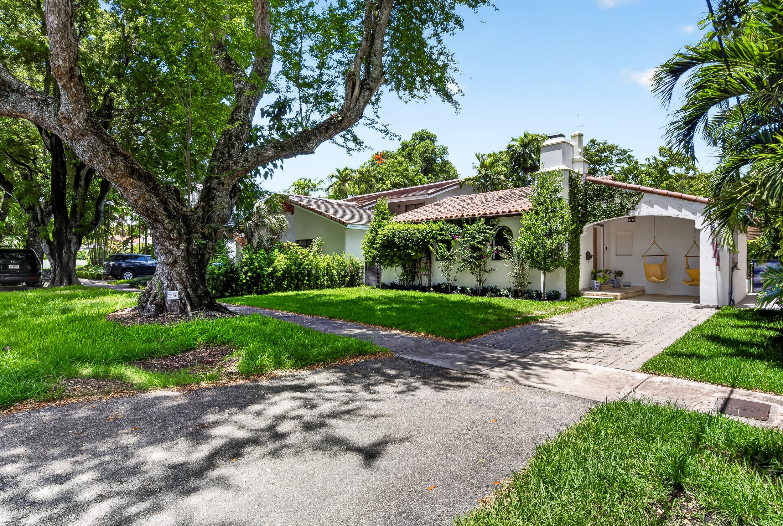 A rare opportunity to own a meticulously renovated Spanish-style home in the heart of Coral Gables. This is not a flip — every material was sourced and every detail was intentional. The result is a home that cannot be replicated.  The great room is the heart of the house and immediately tells you what kind of property this is. Soaring cathedral ceilings clad in original pecky cypress and old Florida pine, exposed wood trusses, and ornate antique corbels create a space that is both dramatic and deeply warm. A book-matched albesia wood mantle anchors the wood-burning fireplace as a true focal point — the grain pattern and natural edge make it a functional piece of art. Arched doorways, dual chandelier pendants, and recessed lighting complete the space. The chef's kitchen is bold and built to perform. Matte black shaker cabinets with brass hardware frame the room, while marble countertops and a farmhouse sink with brass faucet keep it refined. Appliances are top-tier: Sub-Zero refrigerator, Thermador gas range, and matching Thermador double wall oven with built-in microwave. A glass-door pantry provides generous storage, and the striking black-and-white patterned tile floor grounds the whole design. Exposed beams carry the living room's aesthetic seamlessly into the kitchen.  The dining area is a nod to craftsmanship from another hemisphere — imported Mexican terracotta tile flooring, custom imported woodwork details, and a wide arched opening connecting the space to the living room make this an entertainer's dream layout.  Luxury vinyl plank flooring runs through the main living areas, combining the warmth of hardwood aesthetics with durability built for South Florida living.  The primary suite offers a genuine retreat — vaulted beamed ceilings, arched entry, wall-mounted TV, and direct access to one of the most impressive walk-in closets you'll find at this price point. Custom floor-to-ceiling wood built-ins with dedicated shoe display, drawer banks, and full hanging sections sit over large-format marble porcelain tile.  The primary bath carries the same level of finish: Carrara marble countertops, polished brass widespread faucets, and classic white subway tile throughout.  Outside, the home delivers privacy and beauty in equal measure. A deep backyard with mature tropical landscaping and a covered pergola wrapped in lush greenery creates an outdoor living space that feels like a private escape. The front elevation is pure Coral Gables — white stucco, clay tile roof, bougainvillea climbing the façade, and a covered porte-cochère entrance with hanging macramé swing chairs flanking a solid wood front door framed in hand-painted Talavera tile.