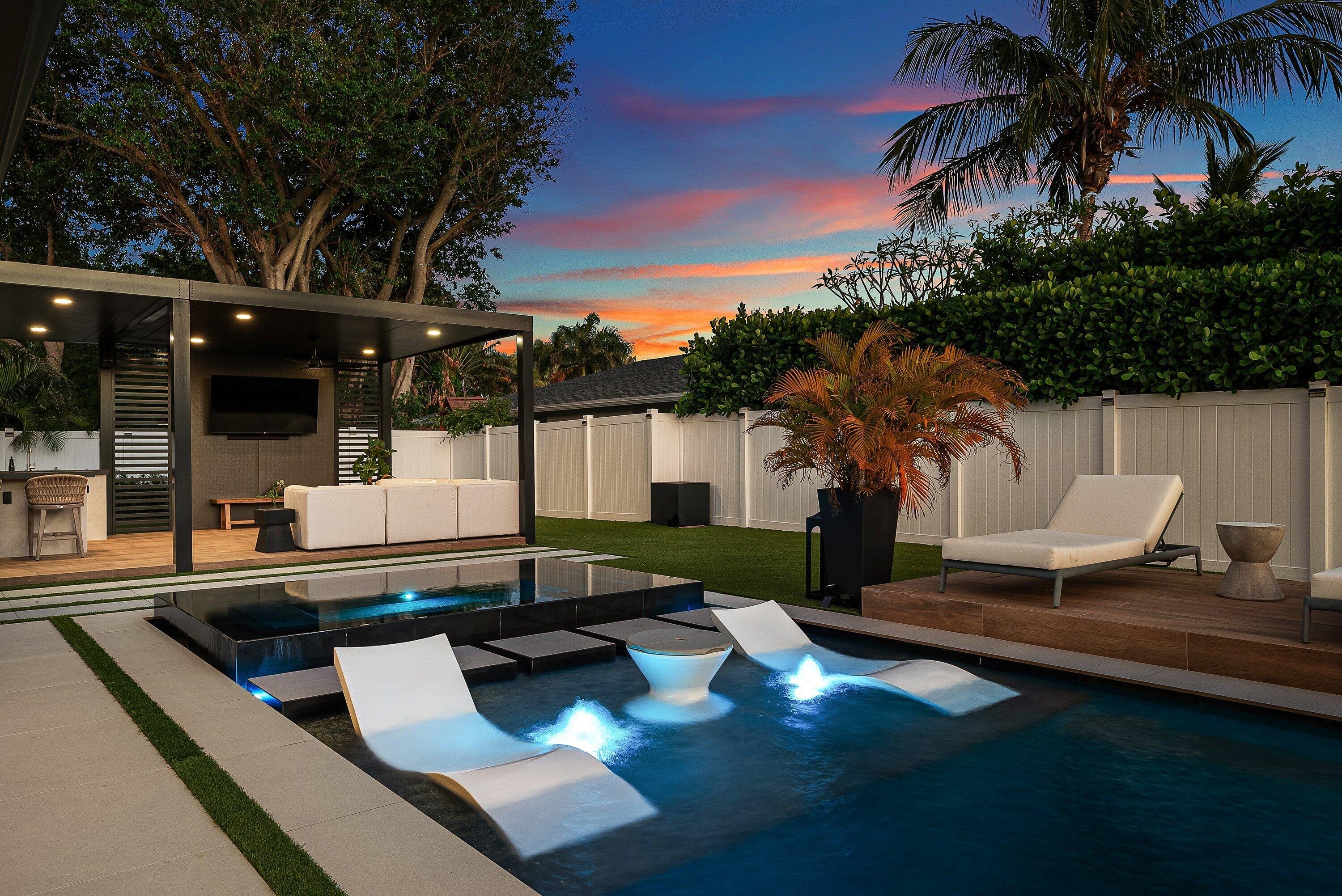 Introducing a striking contemporary residence that seamlessly blends modern design with resort-style living. Thoughtfully crafted with the finest finishes throughout, this home immediately impresses with oversized 48" x 48" porcelain tile flooring, soaring volume ceilings, and sleek architectural details that create a light-filled, open atmosphere. Dimmable LED lighting and linear A/C vents enhance the clean, sophisticated aesthetic, while black hurricane-impact windows and doors provide both style and peace of mind.  At the heart of the home, a showstopping chef's kitchen is designed for both everyday living and elevated entertaining. Custom matte black cabinetry with integrated shelving and built-in outlets is paired with a dramatic Taj Mahal quartzite waterfall island and matching integrated sink. Leathered black quartzite countertops and a full backsplash add depth and texture, while a premium ZLINE appliance package with gas cooktop completes the space. A separate bar area with custom shelving and a wine refrigerator offers the perfect setting for hosting.  The primary suite is a private retreat, featuring a spa-inspired bathroom with an oversized soaking tub, dual shower heads, and a stunning picture window overlooking a tranquil garden framed by a privacy wall. A custom-built walk-in closet with integrated vanity and mirror elevates both functionality and design.  Additional interior highlights include a Jack & Jill bathroom with a custom backlit mirror, three new A/C systems for optimal comfort, a gas water heater, and a spacious garage with epoxy-finished floors.  Step outside to an exceptional backyard designed for true Florida living. The custom pool showcases a glass pebble finish, infinity-edge spa with an oversized champagne spillway, sun shelf with floating steps, and dual-color LED bubblers—all controlled by a full automation system with auto-fill and gas heating. The expansive porcelain pool deck and elevated lounge area provide multiple spaces to relax and entertain, complemented by a 32" gas grill and a fully equipped outdoor entertainment area.  Enhancing the outdoor experience is a 15' x 30' aluminum pergola complete with lighting, ceiling fans, and a media wall with TV, as well as a whole-backyard Sonos speaker system. A 3-hole putting green and artificial turf add a playful yet refined touch, while professionally designed landscaping and low-voltage LED lighting create a lush, private setting.  The exterior is equally impressive with a new concrete paver driveway and a dedicated garden feature area off the primary suite, offering a serene extension of the indoor living space.  This residence is a masterful combination of luxury, innovation, and lifestyle—designed for those who appreciate elevated living and impeccable attention to detail.  The information published and provided including but not limited to prices, measurements, square footages, lot sizes, features, finishes, and calculations are subject to errors, omissions or changes without notice.  All such information should be independently verified.  All parties should perform their own due diligence to verify all information.
