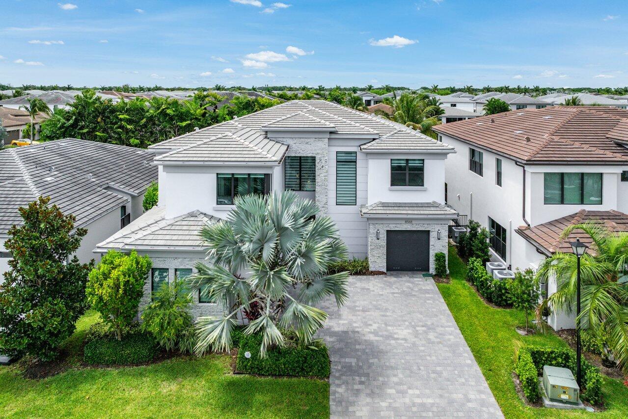 Rarely available and highly sought-after Laguna model in Lotus, featuring over $300,000 in upgrades and situated on an expansive lot with stunning lake views. This exceptional 5-bedroom, 6.5-bath residence offers the ultimate South Florida lifestyle with a huge resort-style pool and spa, spacious 3-car garage, and a sophisticated organic-modern design aesthetic throughout.     From the moment you enter, abundant natural light fills the home as expansive sliding glass doors frame views of the backyard oasis and lake beyond.  Outside, the oversized pool and spa take center stage against a beautiful lake-view backdrop, while the covered patio with a motorized retractable screen, cabana bath, built-in grill, and generous entertaining space create the perfect setting for year-round indoor-outdoor living.     Designed for both everyday living and entertaining, the open-concept floor plan seamlessly blends elegance and functionality. The stunning chef's kitchen features warm custom wood cabinetry, a massive center island, gas cooktop, updated appliances, and extensive storage, flowing effortlessly into the main living areas and formal dining room. A stylish club room with custom built-ins provides additional gathering space, while a first-floor guest suite or office with an en-suite bath and walk-in closet offers flexibility. A custom-built mudroom off the garage adds both style and convenience.     Upstairs, an expansive loft with a custom wood-paneled media wall opens to a large balcony overlooking the pool and lake. The luxurious primary suite is a true retreat, featuring dual walk-in closets and a spa-inspired bath with separate vanities, a dedicated makeup station, freestanding soaking tub, oversized shower, and designer finishes throughout.     A rare opportunity to own one of Lotus' most desirable floor plans on a premium oversized lot with luxury upgrades, exceptional outdoor living, and beautiful lake views.