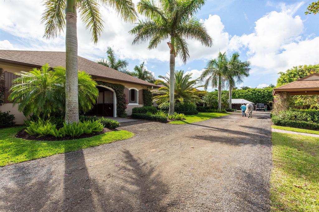 This upgraded professional equestrian facility is located in Palm Beach Point East and is hacking distance to the show via bridle paths. The magnificent, gated property is situated on two parcels totaling 10 acres and boasts a regal, 20-stall barn and residence, new riding arena, 7 paddocks, and a 5-acre derby field. The barn's U-shape design features wide cobblestone aisleways, vaulted wood paneled ceilings with recessed lighting, 20 well-ventilated stalls, 4 hot & cold wash stalls, a large tack room, and a serene, garden courtyard. The expansive 150' by 250' riding arena features new, all-weather footing and is accompanied by a new covered and elevated viewing deck. The recently renovated, main-floor owner's quarters features a living area, dining room, fireplace, screened and covered lanai, and a gorgeous, newly redone pool area with a spacious Travertine tile deck and tropical landscaping. An elegant center staircase in the courtyard leads up to the second level manager's quarters, which offers a spacious deck with a pergola and a bird's eye view of the grounds. Other prominent features include a detached garage with an exterior RV-Hook up, an abundance of parking space, and a stately pavered driveway entrance with automatic gates and designer landscaping.