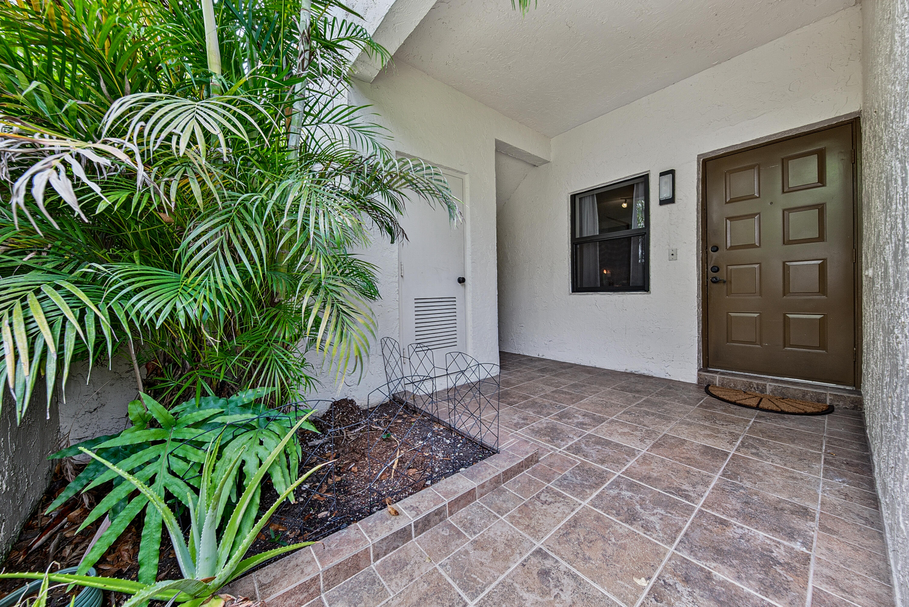 Beautifully appointed and exceptionally spacious, this corner-unit two-bedroom, two-bath condominium offers approximately 1,200 square feet of comfortable, thoughtfully designed living space. The open-concept living and dining areas create an inviting atmosphere ideal for both everyday living and effortless entertaining. Enjoy the serenity of a glass-enclosed patio overlooking lush tropical landscaping, providing both privacy and picturesque views. Impact-resistant windows throughout the residence offer enhanced security, noise reduction, and improved energy efficiency. A charming front patio provides additional storage space and a tranquil setting to relax and enjoy the evening breeze. Residents also enjoy full access to The Township's outstanding resort-style amenities, including tennis