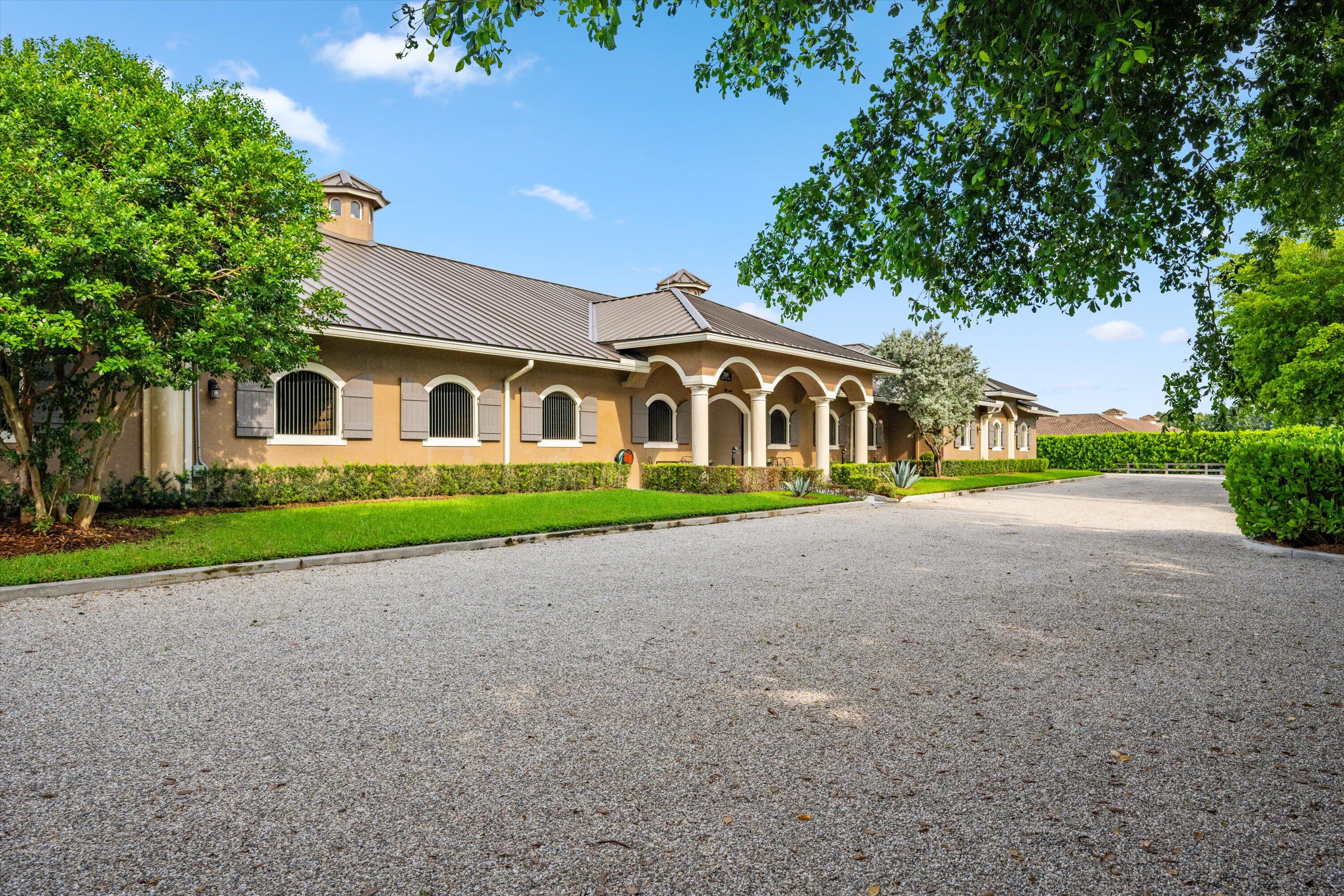 Situated within the gates of Grand Prix Village this 20 stall stable was designed and maintained by a top equestrian professional.  Enter into this stunning stable you will be impressed with the beautiful tongue and groove ceilings, brick front stalls and wide aisles. The stable is fully rubber matted, including the stalls. The interior features include; an office with a full bathroom, a large tack room with a kitchen, a second office, separate farrier and veterinary areas, wash and grooming areas, laundry room and secure med room. There are 3 enclosed garages and a flexible space with a full bath that could easily be converted to living quarters. Outside you will discover the 130X240 COVERED ARENA with GGT footing and multiple paddocks.  Please see documents for a full list of amenities. Enter this property through one of three gated driveways which allow for flow of vehicles and ample parking.  As you walk into this stunning stable you will immediately be impressed with the beautiful tongue and groove ceilings, brick front stalls and wide aisles. The stable is fully rubber matted; including the stalls, which feature fans, fly spray system, and full length grated doors and half doors. The interior features include; a lounge/office with a full bathroom, a large tack room with a kitchen, a second office, separate farrier and veterinary areas, wash and grooming areas, laundry room and secure med room. There are 3 enclosed garage/storage spaces, one being oversized and air conditioned. There is a flexible space with a full bath that is currently used as a photography studio but could easily be converted to living quarters.  As you navigate towards the back of the property you will discover the 130 X 240 covered arena with GGT footing and mulitple sand and grass paddocks.  Your privacy and tranquility are protected with a lovely clusia hedge that surrounds the property.