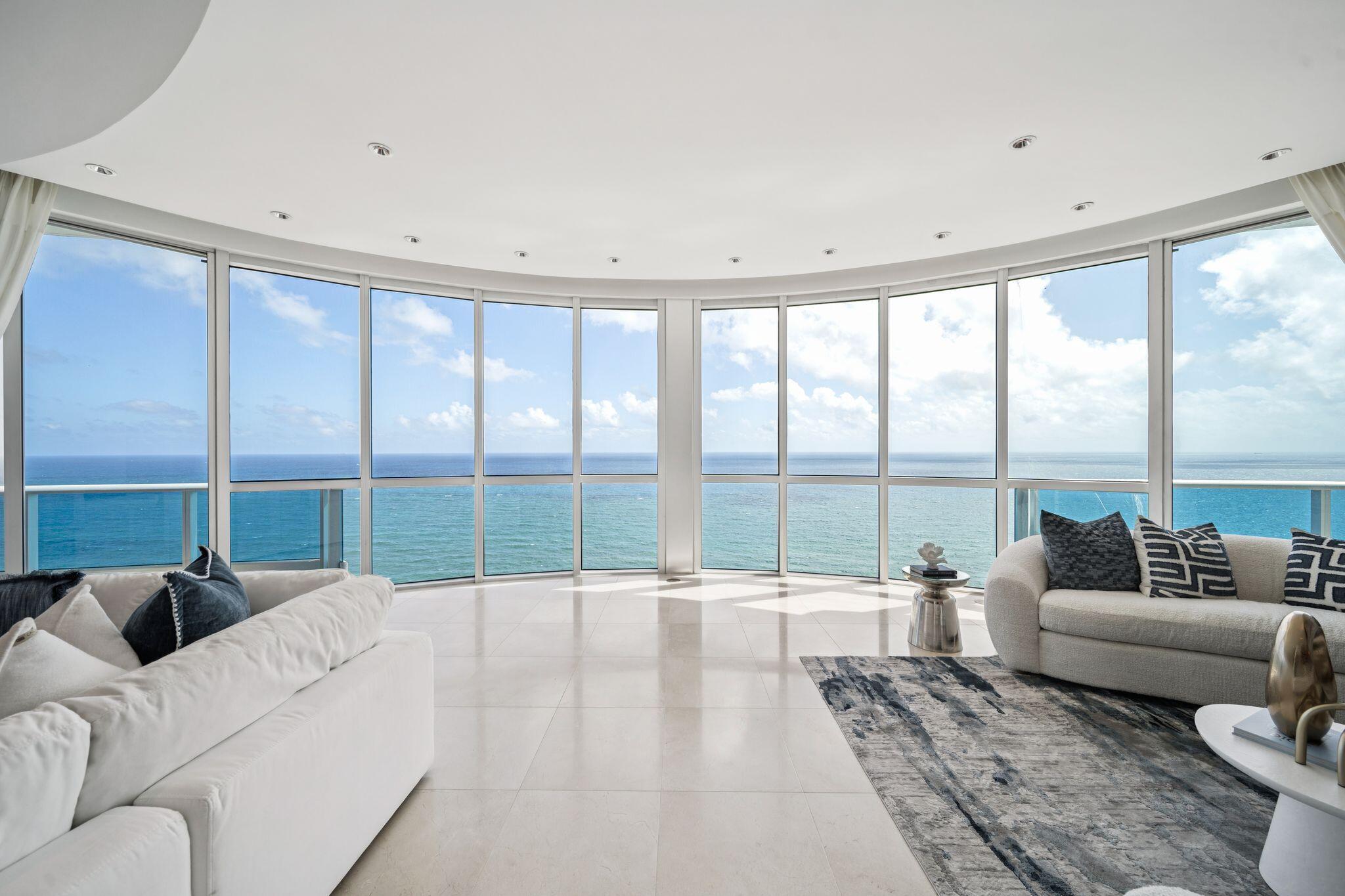 Unobstructed direct oceanfront penthouse commanding the entire southern wing of the building with sweeping coastline views. The tallest PH in the area—clearing all buildings—this one-of-a-kind residence delivers unmatched privacy on the beach. Private elevator access from your street-level garage opens to a dramatic two-story volume ceiling home in the sky, anchored by a sculptural staircase and stunning full-height radial glass wall framing the Atlantic. Custom curving walls and uninterrupted sightline stretches make for a truly architectural flowing floor plan. Eight wraparound balconies capture direct east, south, and west exposures with ocean, sunset, and city views. Set within an extremely amenity-driven luxury building, this rare PH opportunity is the trophy property of the area