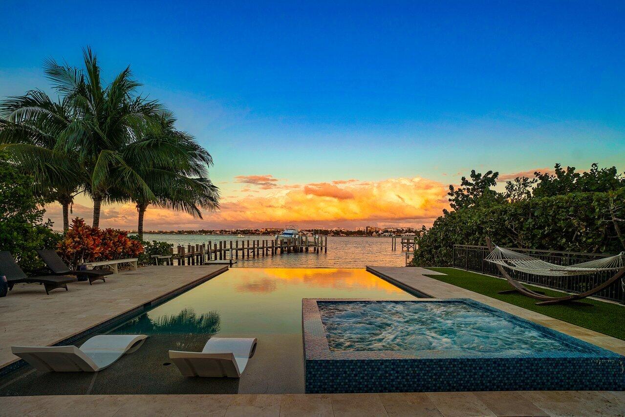 Experience waterfront luxury in this newly renovated direct Intracoastal home. Enjoy breathtaking views from the heated infinity-edge pool and spa, just above your private sandy beach. Inside, soaring 30-foot ceilings, marble floors, quartz countertops, Viking appliances, and designer finishes elevate every space. The grand primary suite features dual walk-in closets, a free-standing tub, and a private patio with panoramic water views. Updates include custom lighting, a quartz fireplace, custom closets, and Gray Malin wallpaper. A guest cottage with a kitchen sits off the gated courtyard. Impact windows, smart home technology, and a security system make it easy to monitor and control your home remotely. Dock your boat on the lift and walk to Old Key Lime House, Eau Resort, or the beach.