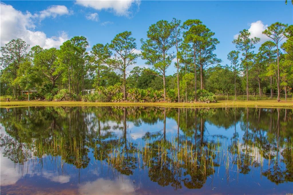 Discover your perfect oasis on this exquisite 5-acre tract! You'll fall in love with this property after seeing the stunning aerial photos. It features a beautiful artesian well-fed 1/4-acre pond, ideal for both leisure and outdoor activities. The spacious barn/storage building, measuring 48x24, comes equipped with three sliding door openings (11 ft wide x 10 ft high), making it perfect for all your equipment and storage needs.   Additionally, the covered "lean-to" measures 35x14 and rises 9 ft in the middle, offering great versatility. The entire property is completely fenced and includes a separate well with a timer, ensuring your palm trees around the pond thrive beautifully. Plus, a generator is provided to run the existing freshwater well, adding convenience to your lifestyle.