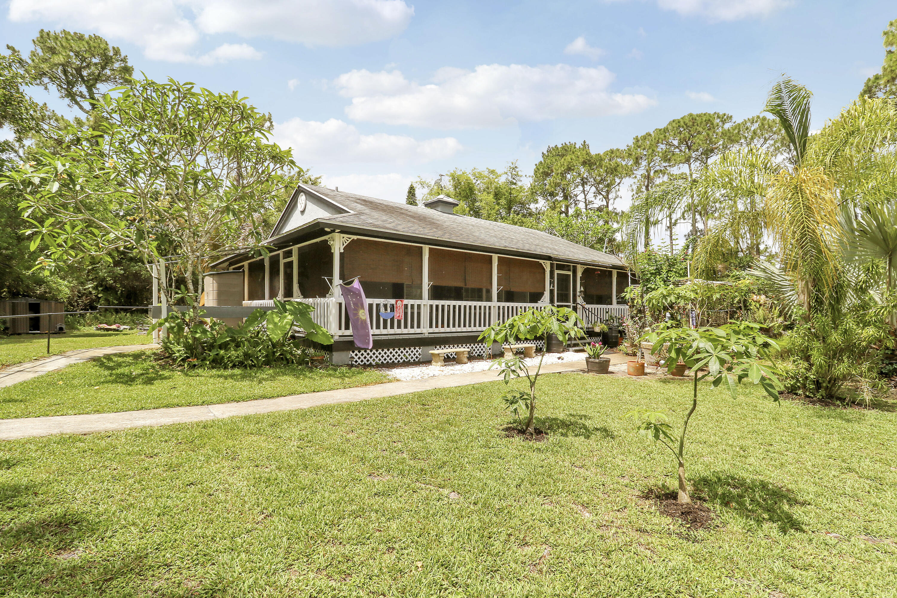 Welcome to 17146 79th Court N in Loxahatchee, where privacy, charm, and peaceful surroundings come together to create your own hidden retreat. Surrounded by lush greenery, this charming 2-bedroom, 2-bathroom Key West-style bungalow offers a setting that feels like an everyday escape with absolute privacy.  From the moment you arrive, you'll appreciate the spacious screened-in wraparound porch, perfect for morning coffee, relaxing evenings, or enjoying the peaceful surroundings. Inside, vaulted ceilings and an open floor plan create a bright and open feel with comfortable living space throughout. The kitchen features granite countertops and newer appliances, blending style and functionality.  Step outside to your private backyard oasis featuring a sparkling solar-heated pool and covered lounge area, ideal for entertaining or unwinding in your own tropical setting with an abundance of fruit trees and tropical plants . Additional updates include a 2015 roof, 2023 A/C system, 2022 water heater, and brand new dishwasher. The spacious primary suite overlooks the pool and the primary bathroom features a jacuzzi tub, creating the perfect place to relax at the end of the day. Located on a quiet road directly across from Temple Park, this home offers the perfect balance of privacy and convenience. You truly need to see this property in person to appreciate all of its charm and unique appeal.