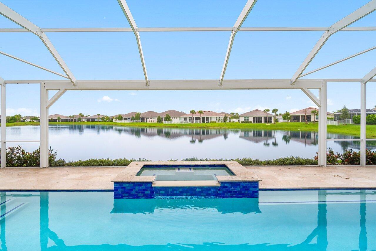 Lakefront Estate with Over $290,000 in Upgrades | Del Webb at Tradition Experience luxury living at its finest in this lakefront estate located within the prestigious 55+ gated community of Del Webb at Tradition. Expertly crafted and enhanced with over $290,000 in premium upgrades, this residence combines timeless elegance with modern comfort. Offering 3 bedrooms, 3.5 baths, a flex room/office, and an extended 3-car garage, the home showcases an inviting open floor plan ideal for entertaining. The owner's suite features tray ceilings, tranquil water views, and a spa-inspired bath with dual vanities, an oversized walk-in shower, and a spacious custom closet with direct access to the laundry room. At the heart of the home, a grand gathering room opens to a chef's kitchen boasting a large... island, granite countertops, upgraded stainless-steel appliances and cabinetry, a wine cooler, elegant tiled backsplash, and a walk-in pantry. Zero-corner impact sliders fully open to merge indoor and outdoor living, revealing a covered lanai with summer kitchen, a large screened pool with heated spa overlooking the lake, and panoramic screening and water views. Additional highlights include upgraded faux-wood tile flooring throughout, custom window treatments, custom closets in every room, a custom drop zone off the garage entry, plywood flooring in the attic, and an enhanced landscape and lighting package. This remarkable property embodies the best of Florida living luxurious, effortless, and ideally situated in one of Tradition's most sought-after active-adult communities.