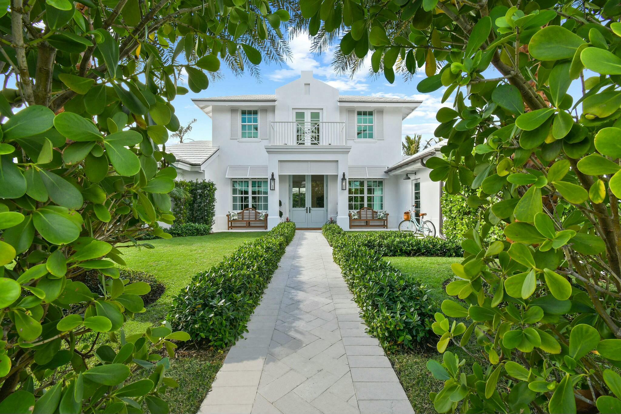 Step into a rare opportunity to own one of the most remarkable interior homes in Jupiter Inlet Colony—a luxurious sanctuary that seamlessly combines high-end design with timeless coastal charm. This home underwent a complete transformation in late 2021, resulting in a masterpiece of refined elegance. The white exterior, inspired by Cape Dutch architecture, is adorned with Bevolo gas lanterns, towering Sylvester palms, lush Bermuda grass, and meticulously maintained Clusia hedges, creating an inviting yet private oasis in this sought-after beachside community. Every element, from the custom Chippendale stairwell to the exquisite Urban Electric and Palecek lighting, has been thoughtfully curated to offer a one-of-a-kind coastal living experience. The interior features expansive, light-filled living spaces enhanced by nickel joint shiplap, coffered ceilings, a whitewashed Pecky Cypress fireplace, and wide plank white oak flooring. At the heart of the home is a stunning gourmet kitchen, anchored by a Lacanche range and a Calacatta Gold marble island, ideal for both entertaining and daily living. A built-in bar area, marble backsplash, inset cabinetry, and dual dishwashers complete the kitchen's flawless design. The dining room flows effortlessly into the spacious living and family rooms, providing a perfect setting for hosting gatherings or enjoying quiet family moments. The main floor boasts luxurious primary and guest suites, each featuring beautifully appointed bathrooms and walk-in closets. Upstairs, two oversized ensuite bedrooms and a cozy sitting area lead to a balcony overlooking the property's lush front yard, offering a serene escape.
The exterior is a private haven, enclosed by a stucco wall and 10-foot hedges. The manicured backyard features an idyllic turf lawn, a gunite pool, a custom 30-foot retractable awning, an outdoor shower, and even a putting greenall accessible through floor-to-ceiling glass doors. This home is truly move-in ready, blending modern conveniences with timeless sophistication. Nestled on the southern tip of Jupiter Island, Jupiter Inlet Colony is a picturesque enclave in Palm Beach County, offering unmatched serenity and exclusivity. This charming community spans less than 0.2 square miles and is bordered by the Atlantic Ocean, the Intracoastal Waterway, and the Jupiter Inlet. With pristine beaches, world-class boating, fishing, and water sports, it's an idyllic setting for coastal living. Safety and peace of mind are paramount, with the town's dedicated police department ensuring a secure environment.
If you're searching for a home that combines elegance, style, and an unbeatable location in one of Florida's most coveted neighborhoods, look no furtherthis extraordinary property is the perfect choice.