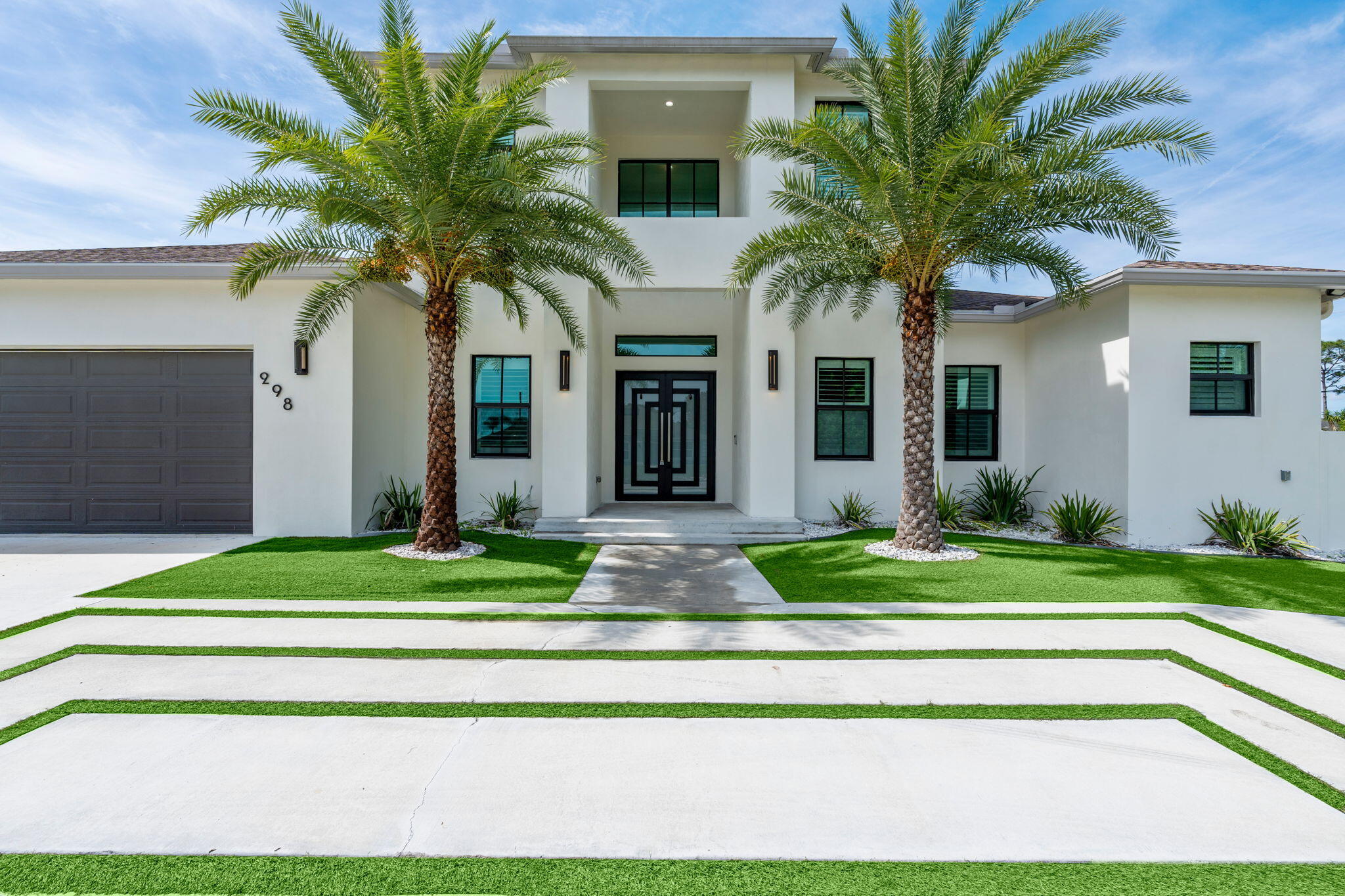Experience contemporary luxury in this stunning two-story home offering over 3,100 sq. ft. of living space with expansive parking for an RV, boat, and all your toys. This 4-bedroom, 4.5-bath residence features a highly desirable FIRST-FLOOR PRIMARY SUITE for added privacy, along with spacious en-suite bedrooms throughout.  Designed with elevated modern finishes, the home showcases porcelain countertops, a custom wet bar, and a fully integrated camera and audio system. The private backyard oasis is built for entertaining with a sparkling saltwater pool, fully equipped summer kitchen, synthetic turf, and elegant tongue-and-groove patio ceilings.  Ideally located just 1.5 miles from public boat ramps with easy river and ocean access, while remaining close to major highways, shopping, & dining