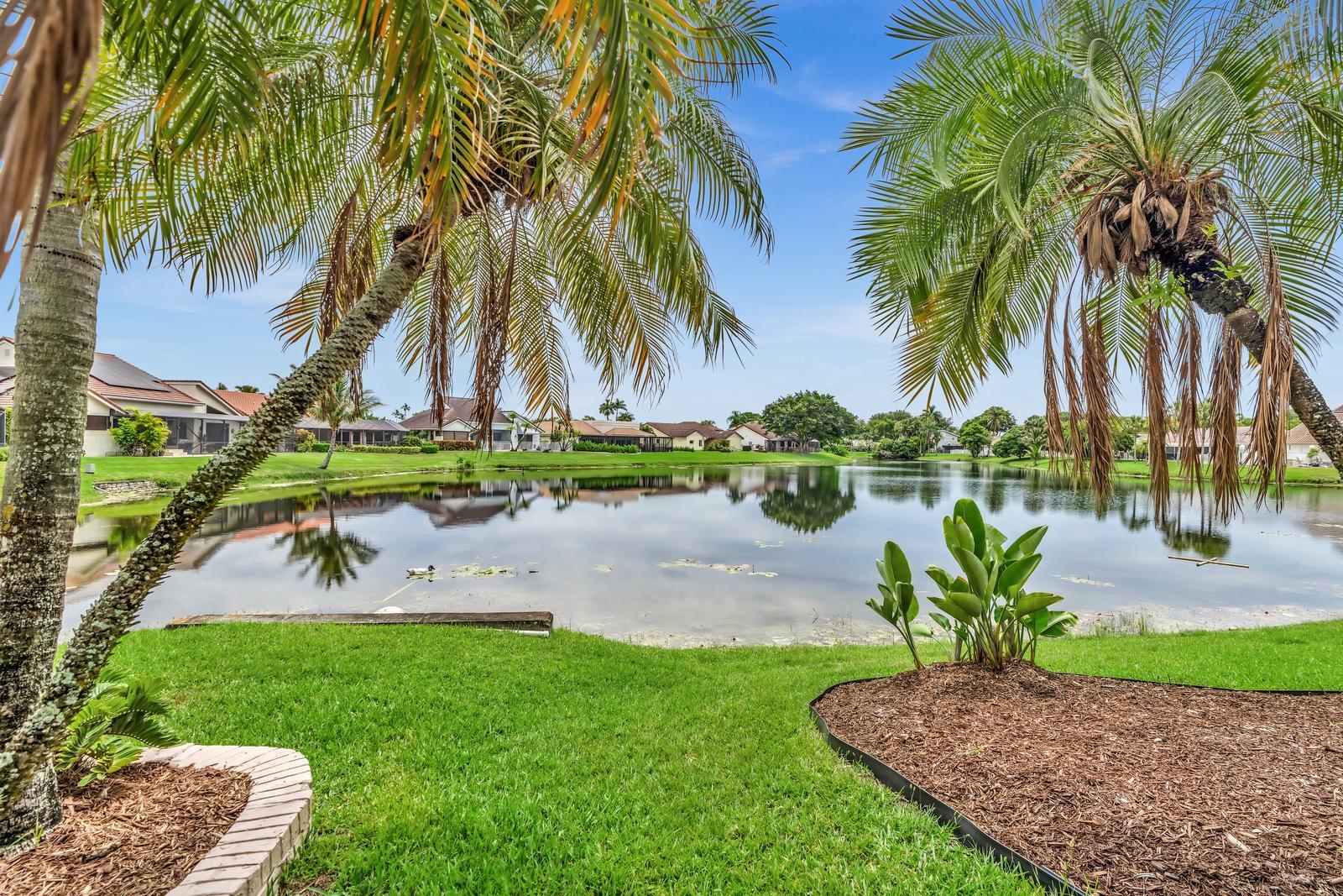 Pristine home with spectacular panoramic long lake views in desirable Palm Ridge at Woodmont Country Club. Move-in ready with open, spacious layout and remodeled kitchen (2021) with breakfast area. Main living areas feature elegant porcelain tile flooring and oak ceilings, plus a built-in Murphy bed for added versatility. Recent updates include dishwasher, refrigerator, washer & dryer (2023), skylights and electric panel with surge protector (2024), A/C only 3 years old, and hot water heater and sprinkler pump replaced in 2025. Accordion hurricane shutters, hurricane-rated garage and pedestrian doors. Oversized lot in quiet community with one entrance/exit. Low HOA $375/year. Golf, tennis, clubhouse and restaurant available pay-as-you-go.