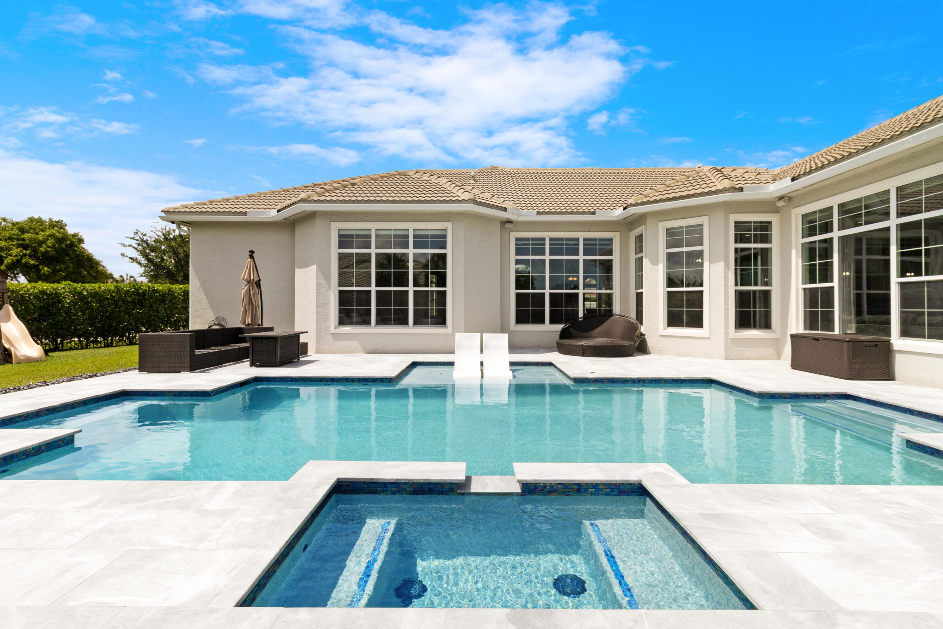 Experience elevated South Florida living in this luxury lakefront estate within the prestigious gated Sterling Ranch community, offering over 4,000 square feet of thoughtfully designed living space, a resort-style saltwater pool, sweeping water views, and exceptional indoor-outdoor living. The home's split floor plan creates exceptional privacy, with a dedicated primary suite and office wing separated from the guest bedrooms. Designed for both entertaining and everyday living, the expansive layout includes two spacious living areas, a formal dining room, breakfast nook, and a chef's kitchen with oversized peninsula seating for four. The kitchen features double wall ovens, designer hood, cooktop, maple cabinetry, granite countertops, built-in desk area, and a large walk-in pantry. Throughout the home, 8-foot interior doors enhance the scale and luxury feel of the space. The luxurious primary suite serves as a private retreat with automatic custom shades, oversized dual walk-in closets, and a spa-inspired bathroom. Two guest bedrooms include private ensuite bathrooms, while the fourth bedroom with adjacent full bath is ideal for guests or multigenerational living. Step outside to a resort-style waterfront backyard featuring a heated and cooled saltwater pool with spa, sun shelf, bubblers, LED lighting, built-in bench seating, and in-water loungers. The covered lanai includes a fully equipped summer kitchen with built-in grill, sink, refrigerator, and Kevlar storm-rated automatic screens, creating seamless indoor-outdoor living year-round. Additional highlights include full impact windows, doors, and garage doors, built-in family room speakers, intercom system, home automation capability, oversized laundry room with direct access to the 3-car garage, custom recessed soffit lighting, outdoor speaker system, elegant aluminum fencing, and professionally maintained landscaping. Conveniently located near shopping, dining, entertainment, and major highways, this Sterling Ranch lakefront home offers a rare combination of luxury, privacy, modern functionality, and exceptional South Florida lifestyle living.
