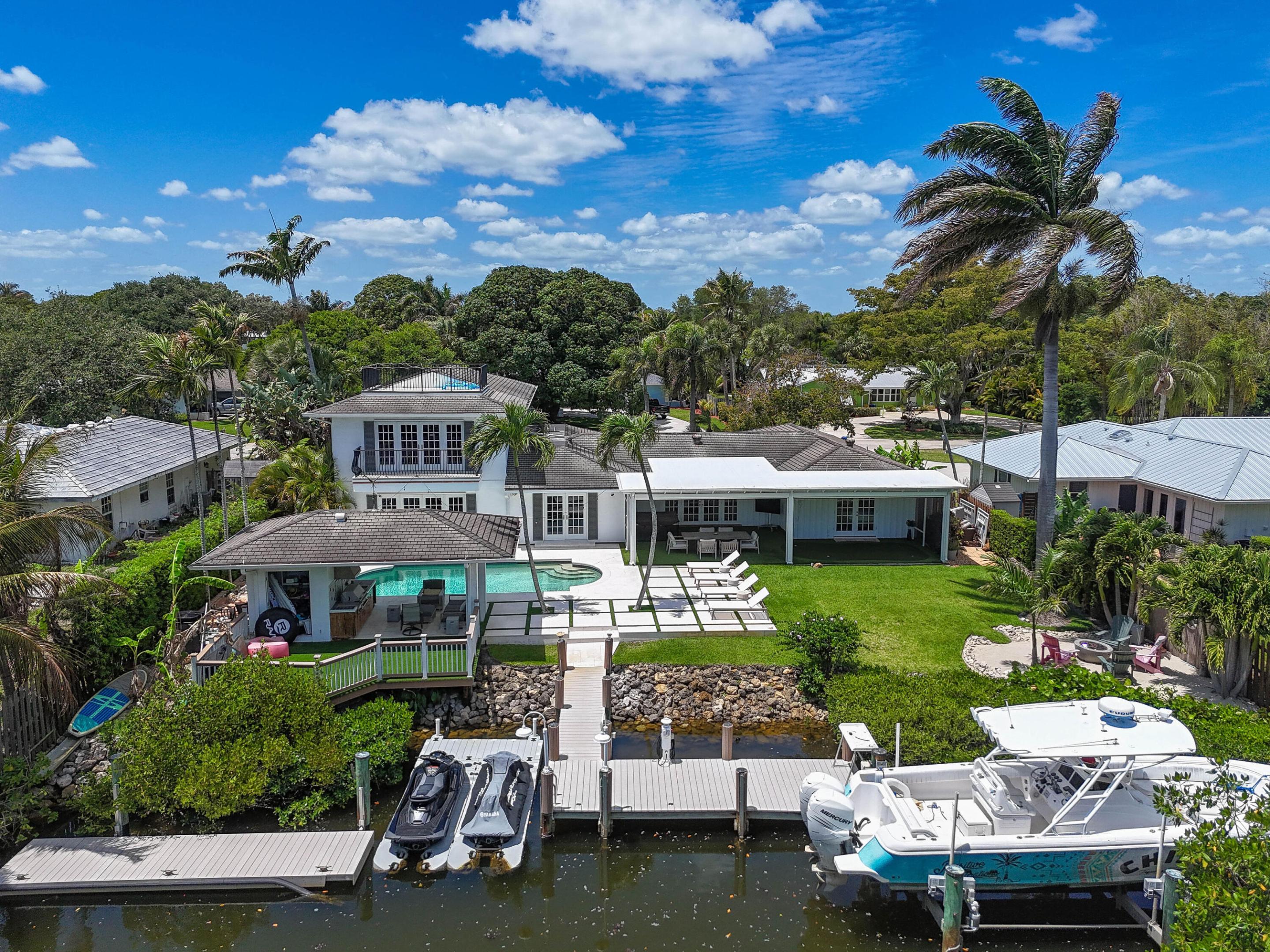 938 Turner Quay is a rare waterfront home offering just under 4,000 sq feet of living space, expansive outdoor living, and exceptional boating amenities, all set on an oversized .47-acre lot with direct ocean and intracoastal access in Jupiter. Thoughtfully designed for both everyday living and large-scale entertaining, the home is equipped with large spaces that connect seamlessly to the backyard. A gracious formal living room welcomes you in, while an oversized family room flows naturally toward the waterfront beyond. At the heart of the home, a substantial chef's kitchen with custom cabinetry, generous prep space and built-in banquet seating creates a natural gathering place, designed both for hosting and everyday family living. Every major living area downstairs was designed to flow to the backyard. Inside, the home has a well-balanced floor plan featuring two private primary suites. The downstairs primary is the entire wing of the left side of the home, vaulted ceilings, french doors leading outside, oversize walk in closet, and large bathroom with a separate shower and soaking tub. The upstairs primary suite has its own private balcony overlooking west-facing water views, a crows nest which allows for direct river and ocean views, walk in closet and large bathroom. The additional guest bedrooms provide comfortable accommodations for family and visitors; both have ensuite bathrooms. Outside, the property transforms into a one-of-a-kind backyard with no homes across the canal allowing for complete privacy. A screened-in lanai with automated screens, astro turf putting green, and multiple covered lounging areas extends the living experience year-round, while the covered outdoor kitchen, dining and seating areas, and cabana bath create the perfect setting for entertaining by the pool. The private pool is framed by mature tropical landscaping and expansive lawn space rarely found on waterfront properties of this caliber. For the boating enthusiast, the property is equally compelling. Two separate docks—including a floating dock, a dock with boat lift, and dedicated jet ski docks—provide exceptional flexibility for waterfront recreation, all with direct access to the intracoastal and ocean beyond. A waterfront fire pit creates an incredible focal point at the edge of the property, offering a setting to enjoy sunsets over the water after a day on the boat.  Further enhancing the home are a two-car garage, generous circular driveway, and the privacy and presence afforded by the oversized lot. Combining premier dockage, expansive grounds, multiple indoor and outdoor living spaces, and a layout designed to live like a true waterfront home, 938 Turner Quay offers a rare opportunity to enjoy the very best of Jupiter waterfront living.