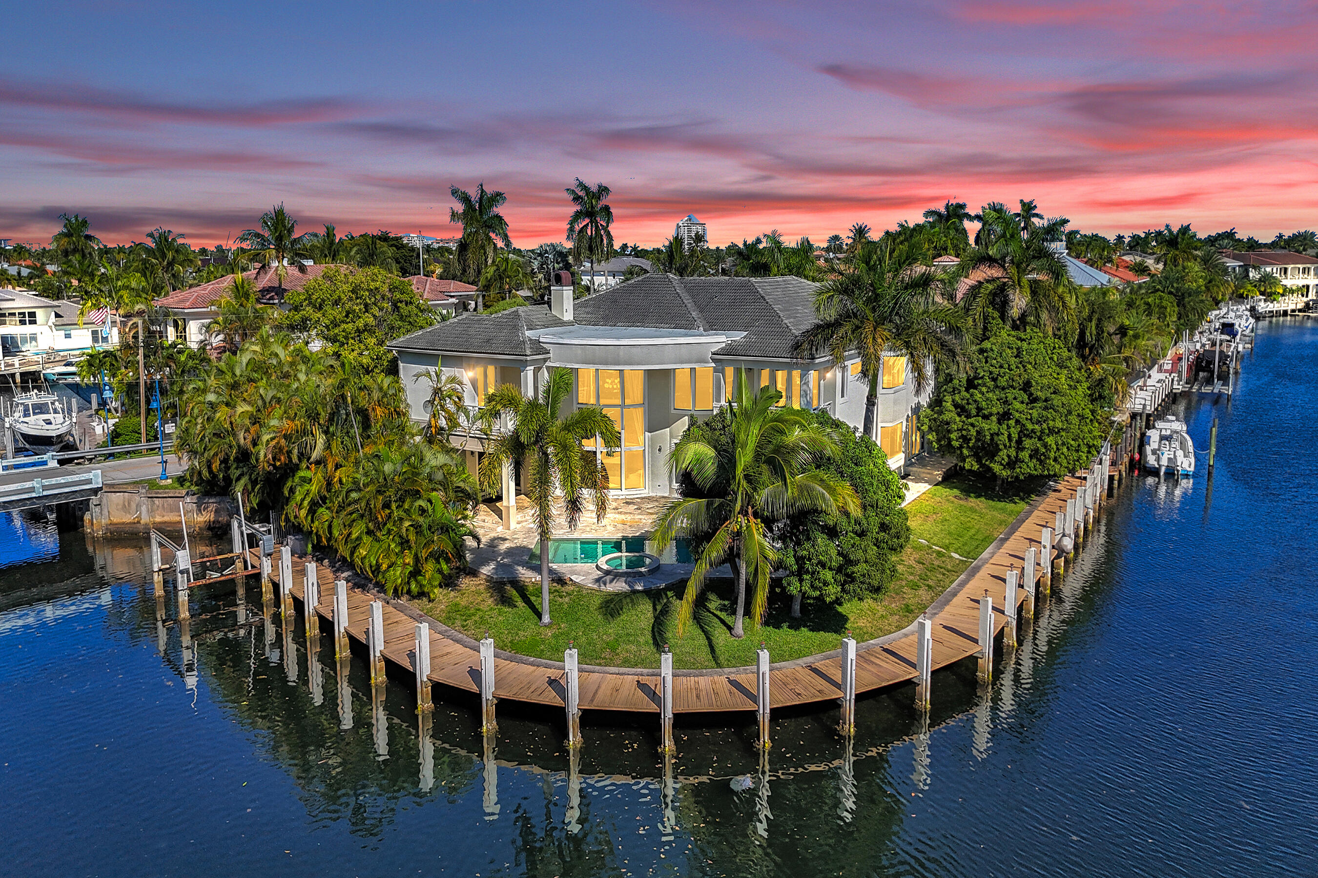 Welcome to your Gated WATERFRONT Point Lot Estate with 223' of deep water frontage! Set along one of Lighthouse Point's most coveted island streets, this  5 Bed + Office + 6 Baths + 3 Car Garage + 1 Car Carport + Pool distinguished waterfront estate presents a rare convergence of architectural refinement, privacy, and premier yachting access. This residence is thoughtfully designed for those who value seamless indoor-outdoor living and life on the water, offering an elevated coastal lifestyle defined by elegance, scale, and quiet exclusivity.  A grand entry opens to a formal living room with floor to ceiling windows, coffered ceilings and fireplace, flowing seamlessly into a formal dining room with a beverage center, creating an elegant backdrop for sophisticated gathering. The chef's kitchen is the heart of the home, featuring a Thermador Stainless Steel 6 Burner/Griddle gas cooktop, double ovens, dishwasher and microwave, a Sub Zero Refrigerator and Freezer, an oversized island, bar seating, and effortless connection to the expansive family room with a separate dining area perfect for watching the sunrise. The residence features five bedrooms, all en suite, including three primary suites, and two generously appointed bedrooms suites (One Primary Suite and one Bedroom Suite with Cabana Bath are located on the first floor) as well as a richly appointed office with a private balcony that offers flexibility as a convertible bedroom or executive workspace. In total, the home offers five full baths, a first-floor powder bath all thoughtfully designed for both comfort and entertaining. The primary owner's suite occupies a premier second floor position and is a private retreat, showcasing a large balcony with spiral staircase access to the pool and patio, evoking the ease of yacht-to-home living. Step into your spa inspired bath with dual vanities, a whirlpool tub, separate his-and-hers water closets, and a custom walk-in closet with island and built-ins. Unwind after a long day on the water or enjoy private screenings in your entertainment and media lounge with custom cabinetry, refrigerator, sink, in-wall speakers, and glass doors to shut out the world while you relax in your retreat. An ELEVATOR services all levels, while both upstairs and downstairs laundry rooms add everyday convenience. The home is complemented by a three car garage plus an additional carport, offering ample parking and storage. Impact windows throughout ensure peace of mind in all seasons.
Enjoy the TRANQUIL covered patios as the estate unfolds into a SUBSTANTIAL marble pool deck with a PICTURE-PERFECT tropical resort style pool and built in hot tub that  is surrounded by lush landscaping. The oversize lot along with your private dock that wraps around the property provides SUBSTANSIAL room for you, your family, guests and pets to enjoy true South Florida waterfront living. With 223' of water frontage and dock space, there is AMPLE room for your Sportfish, Sport Yacht and Center Console.  Located on a prestigious island street, moments from the Intracoastal and ocean access, this property presents a rare opportunity to secure a  waterfront estate for those who live life on the water. Outdoors, the estate delivers true resort-style waterfront living, with a tropical pool and spa, expansive patio areas, and commanding water views from nearly every angle. The corner-lot orientation provides enhanced privacy, expanded dock potential, and dramatic sightlines, an exceptional advantage for yacht owners. This is a rare opportunity to own a corner lot waterfront estate in one of Lighthouse Point's most desirable island settings where luxury, location, and lifestyle converge.