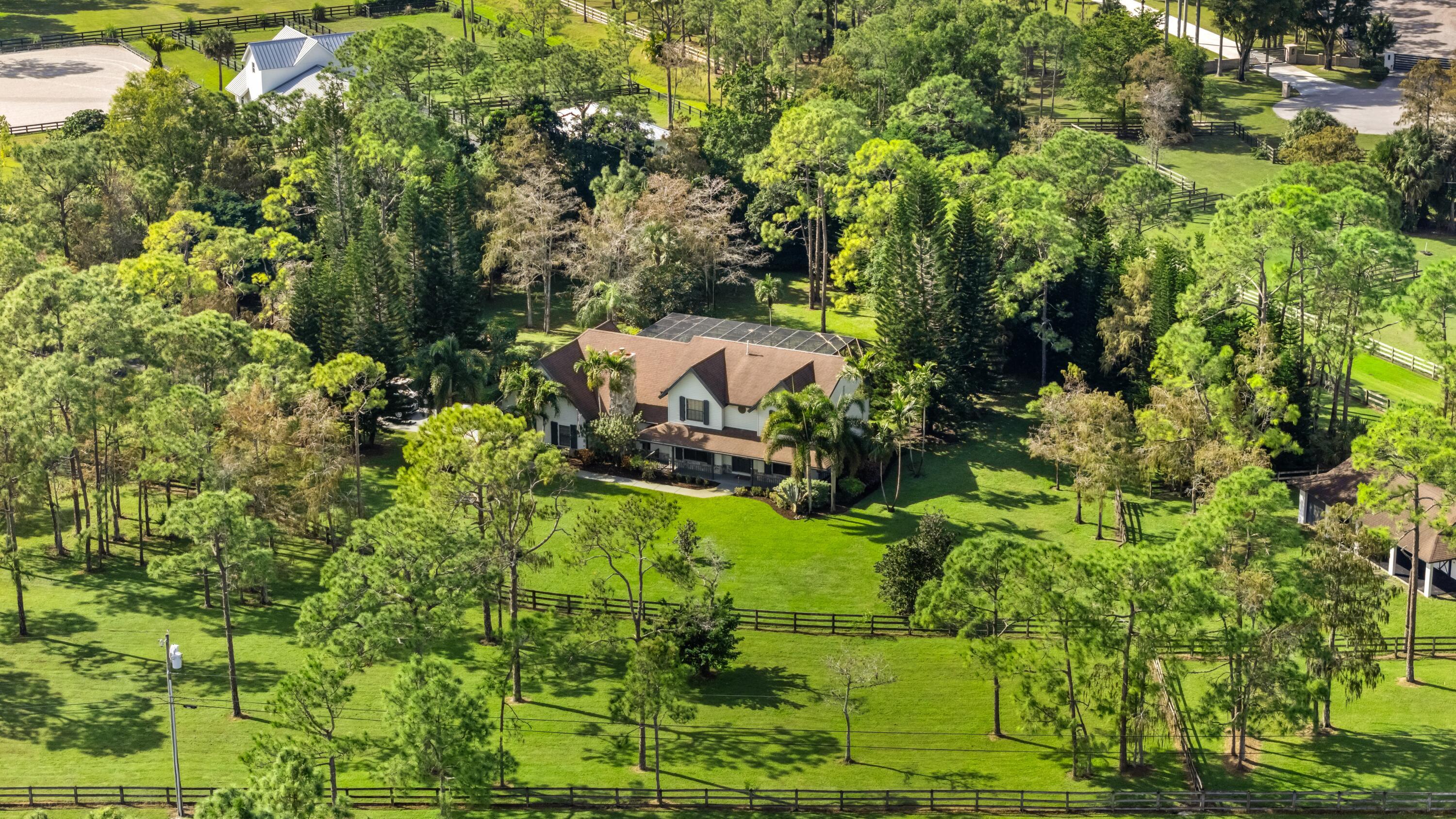 Welcome to Pickwick Farm, a cherished Homeland estate lovingly maintained by the same owner for nearly 30 years. Set on 5+ high-and-dry acres within one of Palm Beach County's premier gated equestrian communities, this classic 5-bed, 3.5-bath Northern-style Colonial is surrounded by towering Northern Pines that provide exceptional privacy, less than 15 minutes from Wellington International and the NPC. Equestrian amenities include a durable 3-stall concrete block barn with tack room, 4 irrigated paddocks, 3 wells, and a desirable corner lot with dual entrances separating residential and horse access. Whether enjoyed as it stands today or transformed into your dream equestrian estate, Pickwick Farm offers an exceptional combination of location, acreage, infrastructure, and potential. Inside, multiple living and dining spaces offer room to gather, while the welcoming family room is anchored by a stately gas fireplace. The kitchen features wood cabinetry, Sub-Zero paneled and stainless-steel appliances, a copper farmhouse sink, and a gas cooktop. Three REME HALO® air purification systems with UV lights enhance indoor air quality throughout the home, while a brand-new washer and dryer and whole-house generator provide added convenience and peace of mind. The screened Caretaker in-floor self-cleaning pool and spa are nestled among the towering pines, creating a peaceful outdoor retreat with exceptional privacy.  While a new owner may choose to update and personalize the residence, its greatest assets are the exceptional homesite, mature landscape, established equestrian improvements, and classic Colonial architecture.