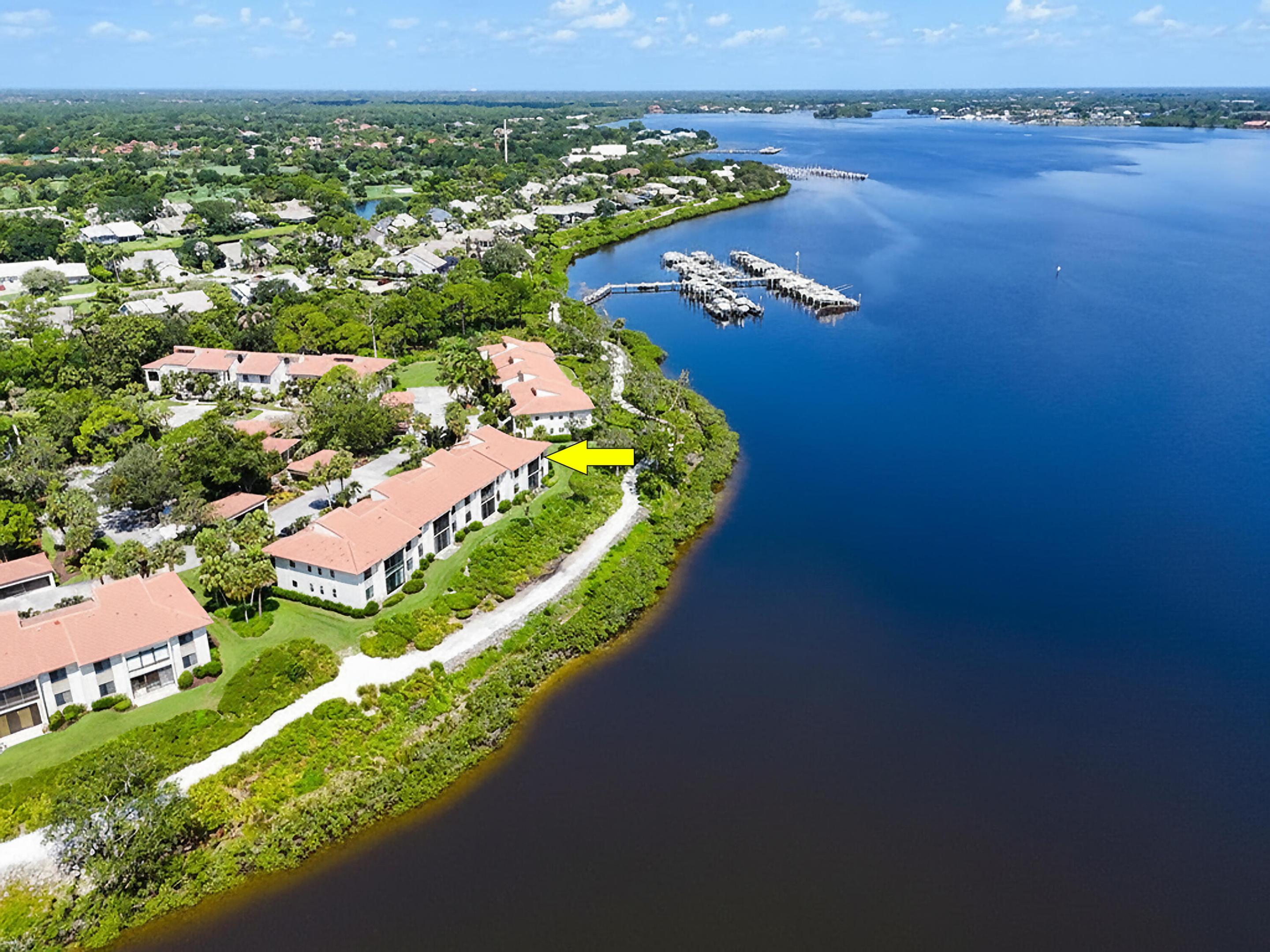 Commanding the widest panoramic views of the St. Lucie River of any Bayhead condo, this exceptional end-unit residence is one of the community's most desirable waterfront offerings. Surrounded by lush tropical landscaping from the welcoming front entry to the expansive rear patio, this private retreat offers a peaceful, secluded setting while showcasing breathtaking river views from nearly every room. Inside, the thoughtfully designed split floor plan offers 1,949 square feet of living space with two spacious bedrooms plus a versatile den that can easily serve as a third bedroom or home office. The main living area is enhanced by soaring vaulted ceilings with beautiful tongue-and-groove detailing, creating an open, airy atmosphere filled with abundant natural light while perfectly framing  the spectacular waterfront backdrop. Recently renovated bathrooms, three closets in the primary suite, a walk-in closet in the guest bedroom, and a custom built-in bar in the den provide exceptional comfort and functionality. Step outside your back door and immerse yourself in the quintessential Florida lifestyle. Enjoy direct access to Harbour Ridge's scenic two-mile nature trail that winds along the picturesque St. Lucie River—perfect for morning walks, evening sunsets, or simply taking in the abundant wildlife. If you keep a boat at the marina, you'll also appreciate the convenience of walking from your residence directly to your boat and being on the water in minutes. Lovingly maintained by its original owner, the home also features a 2013 A/C, 2022 water heater, accordion hurricane shutters, a covered carport with private storage, and an ideal location just steps from the community pool and golf cart storage. Rarely does an end-unit residence combine the widest river views in Bayhead Village, exceptional privacy, and an unparalleled connection to nature, creating an extraordinary opportunity to experience the very best of Harbour Ridge Yacht & Country Club living. Harbour Ridge is one of the most premier private club memberships in all of South Florida, which offers luxurious amenities for all of their members. Whether you enjoy golf, boating, kayaking, paddle boarding, fitness, tennis, pickleball, dining, bird watching, or embracing the natural surrounds of a Certified Audubon Cooperative Sanctuary, Harbour Ridge offers something for everyone. The club also prides themselves by providing their membership an unparalleled level of personalized service across all amenity venues to ensure the highest level of membership experiences throughout the club and community.