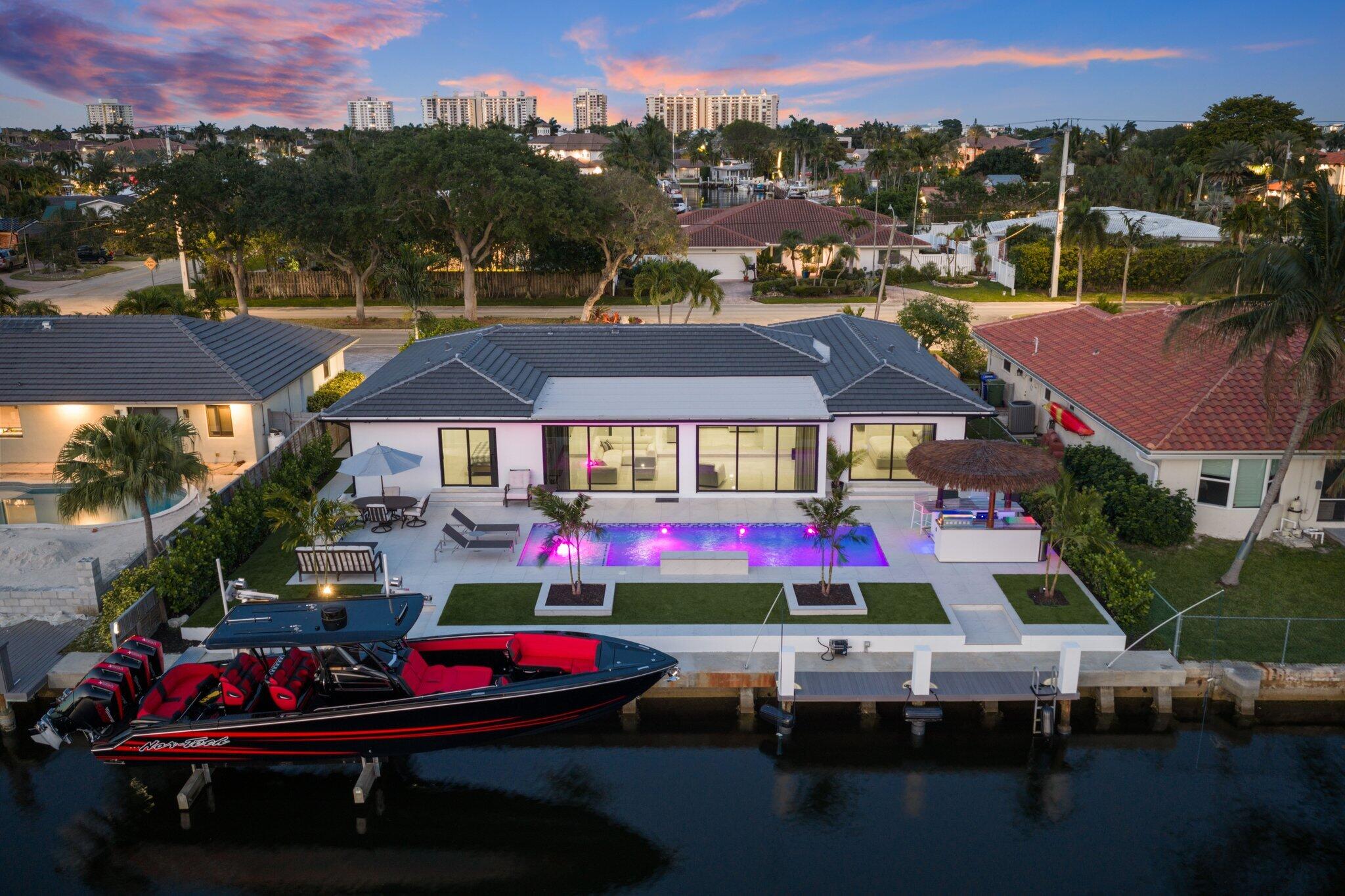80 ft of prime waterfront with dock, 17,000 lb boat lift, elevated seawall, and a stunning infinity pool. The backyard is a true showpiece featuring an outdoor kitchen, tiki hut, turf, and a clean paved entertaining area designed for seamless indoor outdoor living. Inside offers 48x48 porcelain floors, a quartz waterfall island, sleek European style kitchen, higher ceilings, and an open layout. 3 bed, 3 bath with two primary suites, both with water views and private backyard access. Finished with concrete tile roof, impact glass, custom closets, designer baths, circular driveway, and synthetic stucco exterior. Turnkey waterfront with dock, lift, and modern design. The accuracy of all information is deemed reliable but not guaranteed and should be verified by agent/buyer.
