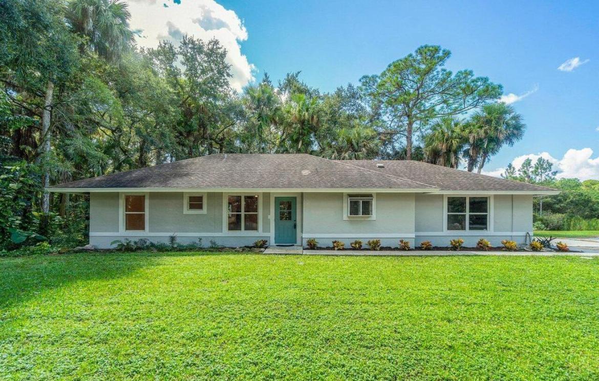 A hidden paradise on the edge of West Palm Beach! Experience old Florida charm on this rare 2.58-acre fully fenced property, surrounded by a peaceful hammock of oak, palm, and pine trees. This beautifully renovated 3-bedroom, 2-bath home features a newer kitchen with updated cabinets, quartz countertops, renovated bathrooms, vaulted ceilings, skylights, and a cozy wood-burning fireplace. The west side of the property offers a barn with attached chicken coop, pastured field, pond, garden space, and a full-size basketball court. Two gates provide convenient access to the circular driveway and wooded area. Additional upgrades include A/C 2018, roof Oct. 2024, knockdown ceilings, and a new well water system. Enjoy mulberry, sour orange, lychee, coconut, bay leaf trees, and more. Steps from J.