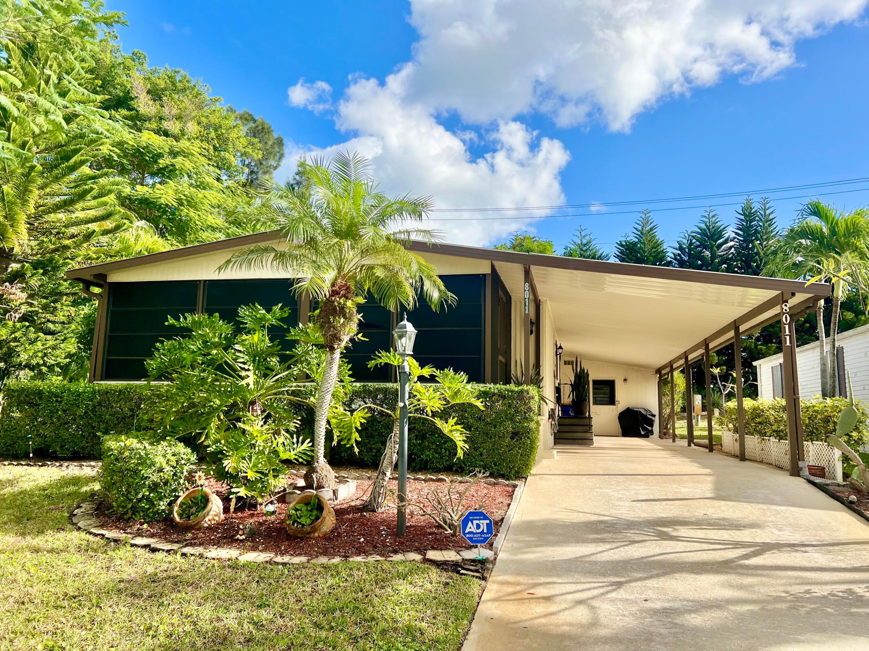 This well maintained home in the Cambridge community is open and spacious with an extremely comfortable, cozy feel! Set slightly higher on a large lot, it is surrounded by mature landscaping. The additional lot space offers many opportunities. The extra long carport can easily fit up to 3 cars, and opens to the utility/storage room with plenty of additional storage space. Highlights include a metal roof, 2021 AC, 2025 water heater, 2022 washer and dryer, new wood laminate flooring and plywood installed in 2018, vapor barrier and strapping that is up to code, and a new water pump for the automatic sprinkler system installed in 2018. Cambridge is a well-maintained, active 55+ community, where you OWN THE LAND! This home is close to Hobe Sound beaches, shopping and restaurants, and next to the public Heritage Ridge golf course.  Located in PHASE 1, you can have your BOAT or RV! AND, ALL pets are welcome!