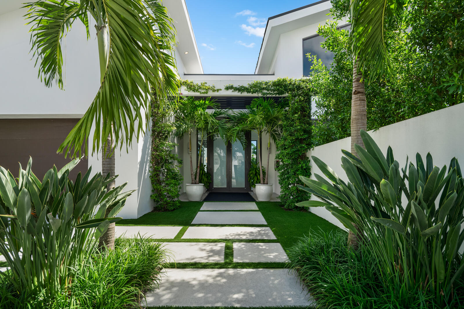 Set on a 9,345± square-foot lot, this SoSo residence combines privacy, thoughtful design, and a prime location near the Intracoastal bike path and Palm Beach Island. This contemporary residence offers 4,690± total square feet with 4 bedrooms, 4 full bathrooms, and a half bathroom. Recent updates, including a new pool, all-new landscaping, a gated entry, and a perimeter wall, enhance privacy and curb appeal while maintaining a streamlined modern aesthetic.

The main living areas are oriented around the pool, creating a natural connection between indoor and outdoor living. The living room features soaring ceilings and expansive sliding glass doors that open east to the pool and west to a terrace and lawn surrounded by mature trees and lush greenery. The kitchen, designed for both cooking and gathering, includes a large island, modern finishes, and a dining area overlooking the pool. Adjacent to the main living spaces, a media room serves as a relaxed extension of the homecomplete with a projector and drop-down screen, ideal for movie nights or informal entertaining.

A modern staircase leads to the primary suite, which spans the upper level. The suite includes two private balconiesone overlooking the pool to the east, the other facing south across the lawnalong with a large walk-in closet, additional built-ins, and a desk area. The bathroom features dual sinks, a freestanding soaking tub, and a large glass-enclosed shower.

Three guest bedrooms are located on the main level, including one with an en-suite bath, while the other two share a hallway bathroom. Additional features include a laundry room with storage, powder room, pool bath, outdoor dining area, and a two-car garage.