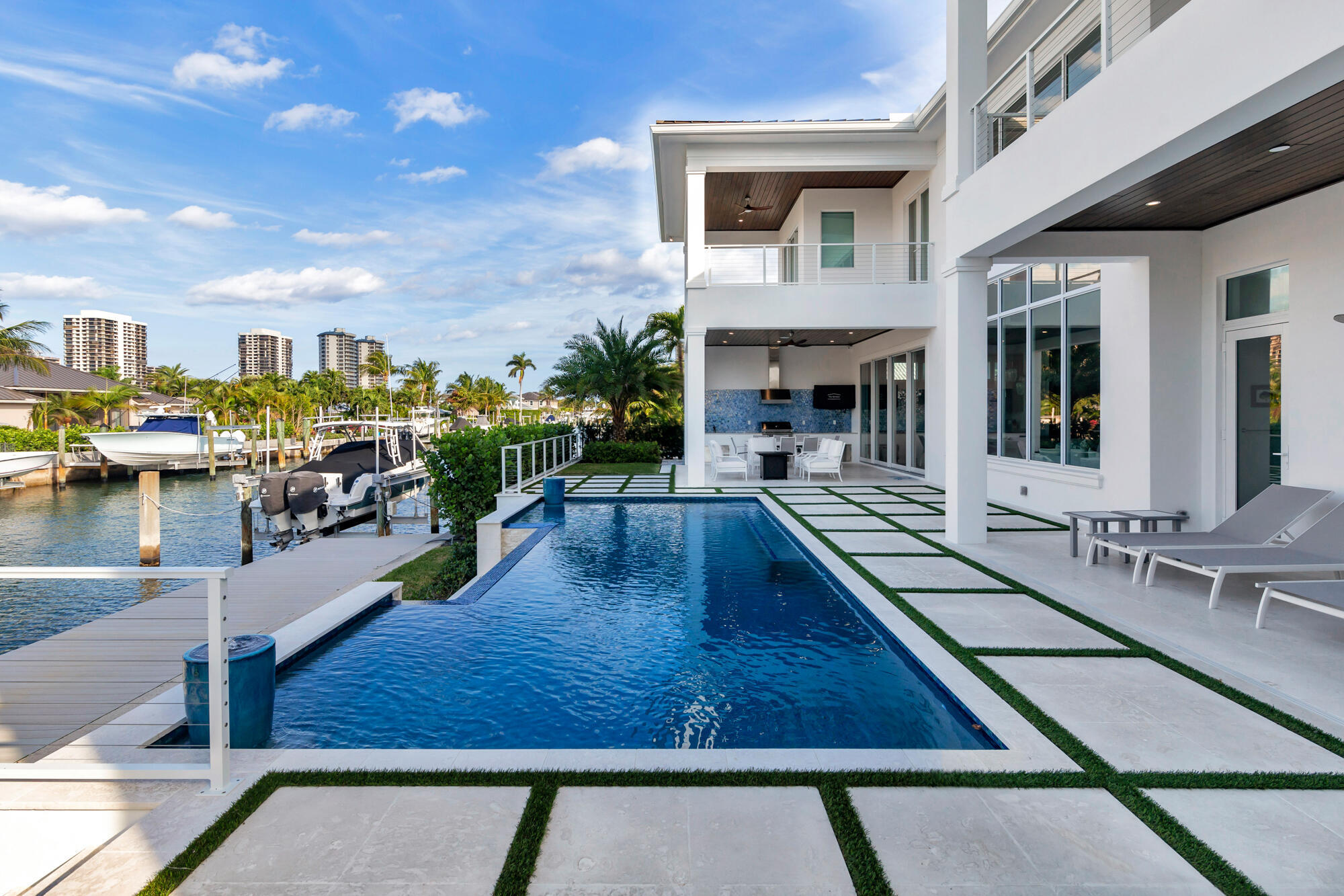 This new construction waterfront residence, completed in 2023, is set on a 100 x 110 lot with 100 feet of water frontage, a private dock, and views of both the canal and Intracoastal.   The home offers 7,246 total square feet with 4 bedrooms, 4.5 bathrooms, with water views from nearly every room.   A foyer leads into the main living spaces, with a study area just off the entry connecting directly to the living room. The living room features floor-to-ceiling glass, a fireplace, and expansive water views. The kitchen connects to both the dining and living areas and is designed for everyday use and entertaining, with a large island, walk-in pantry, custom lighting, water filtration system, wine refrigerator, and a Miele built-in coffee maker. Large doors open to a covered loggia with a summer kitchen overlooking the pool and waterfront.   The first-floor guest suite includes a walk-in closet, direct access to a private guest loggia, and a spacious bathroom with dual sinks and a separate soaking tub.   Upstairs, the primary suite faces the water and features dual walk-in closets, a private covered balcony, wet bar, and a bathroom with dual vanities and a separate soaking tub. Two additional guest suites, each with private balconies and en suite baths, complete the upper level, including one with water views. A loft area and upstairs laundry add additional functionality.   Outdoor living is centered around the heated infinity-edge pool, open patio, covered loggias, summer kitchen, and a powder room with sauna, all positioned along the water. The private dock includes water, electric, and a 14,000 pound boat lift.   Additional features include full impact glass and doors, fully built-out closets throughout, main-level laundry, a three-car garage configuration, and additional driveway parking.