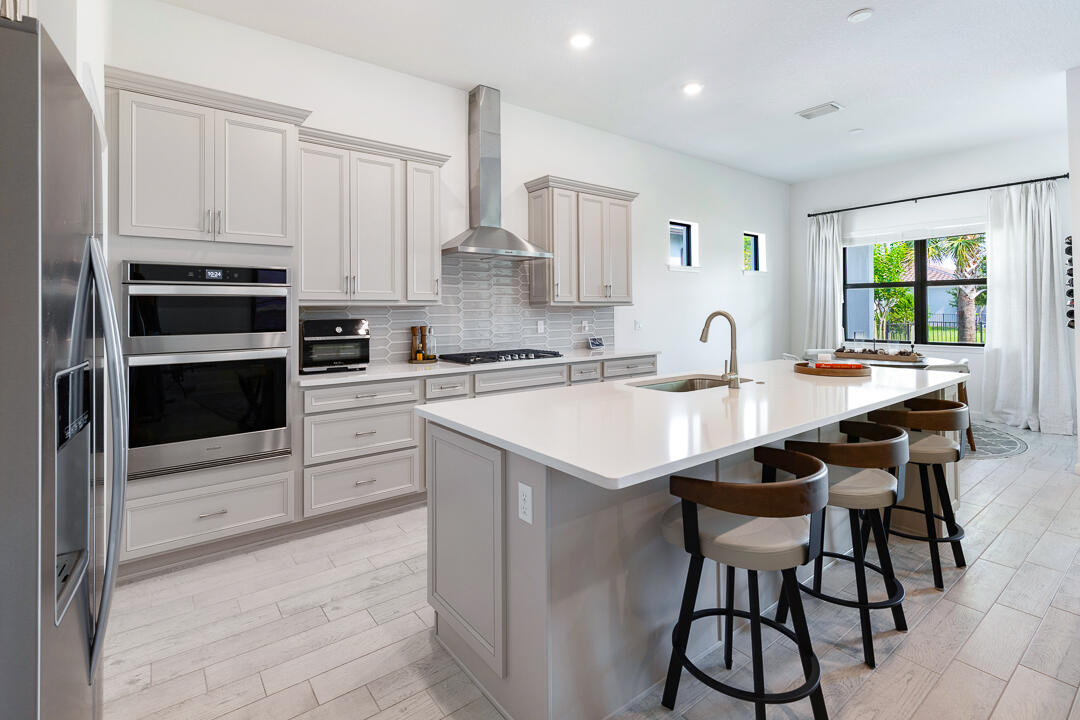 WOW! Move-in ready - loaded with upgrades, this exceptional 3-bedroom, 2.5-bath lakefront home in Veranda Gardens offers luxury and value. The designer kitchen features quartz countertops, stunning backsplash, oversized island with added storage, large walk-in pantry, soft-close cabinetry, glide-out drawers, wall oven, gas cooktop, vent hood, and stainless-steel appliances. The open-concept layout flows to the spacious living area and extended covered paver patio overlooking the lake. The premium primary suite offers tray ceiling, two walk-in closets, and a spa-like bathroom with dual sinks, quartz countertops, and an extended walk-in shower. Impact windows and doors, smart home technology, soaring ceilings, elegant 8' wood doors, wood-look tile flooring throughout. Plus room for a pool! Located in the sought-after gated community of Veranda Gardens renowned for its warmth, hospitality and pet friendliness. Living in Veranda Gardens means access to fantastic amenities including a Clubhouse, resort-like heated pool, spa, lap pool, cabanas, tennis, pickleball, basketball, bocce ball, fitness center, community room, catering kitchen, barefoot bar, BBQ grills, fire pit, grills, playground, dog park, sidewalks, street lights, lawn maintenance and all with a LOW HOA fee. Conveniently located with easy access to the FL Turnpike, I-95, shopping, dining, golf, baseball, the beach, and a new hospital - this home offers the complete package.