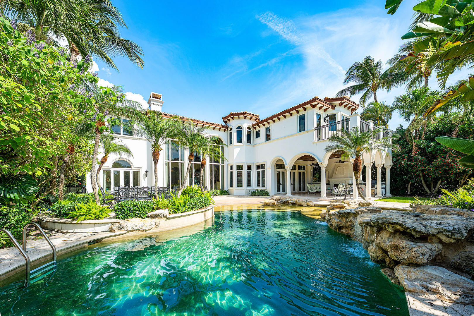 Positioned along the 15th fairway within the prestigious Royal Palm Yacht & Country Club, 1282 Sabal Palm Drive is a private golf course estate defined by timeless architecture, resort-inspired living, and a coveted southeast exposure that fills the residence with natural light from sunrise to sunset. Crafted in 2003 by Bloomfield Construction, the home spans approximately 6,068 square feet of thoughtfully designed interiors, blending elegant entertaining spaces with relaxed everyday comfort. Beyond the stately arrival, the residence unfolds with grand yet inviting proportions. Formal living and dining spaces are complemented by a butler's pantry and a beautifully designed gourmet kitchen featuring premium appliances, a center island, and seamless flow into the home's main gathering areas. The outdoor setting evokes the atmosphere of an exclusive private resort. Surrounded by lush tropical landscaping, the backyard centers around a spectacular beach-entry lagoon-style pool overlooking the manicured fairways beyond. A covered loggia invites year-round outdoor living with a built-in grill, al fresco dining areas, and multiple spaces for entertaining or quiet relaxation beneath the South Florida sky. Privately positioned, the grand primary suite serves as a luxurious retreat, complete with a spacious sitting room, a spa-inspired bath, and a private balcony offering tranquil golf course views. Five bedrooms, five full baths, and a three-and-a-half-car garage provide exceptional comfort and flexibility. Modern conveniences are seamlessly integrated throughout, including Savant home automation with iPad controls, natural gas, impact windows and doors, tankless water heaters, and a generator, delivering effortless living and peace of mind in one of Boca Raton's most prestigious enclaves.