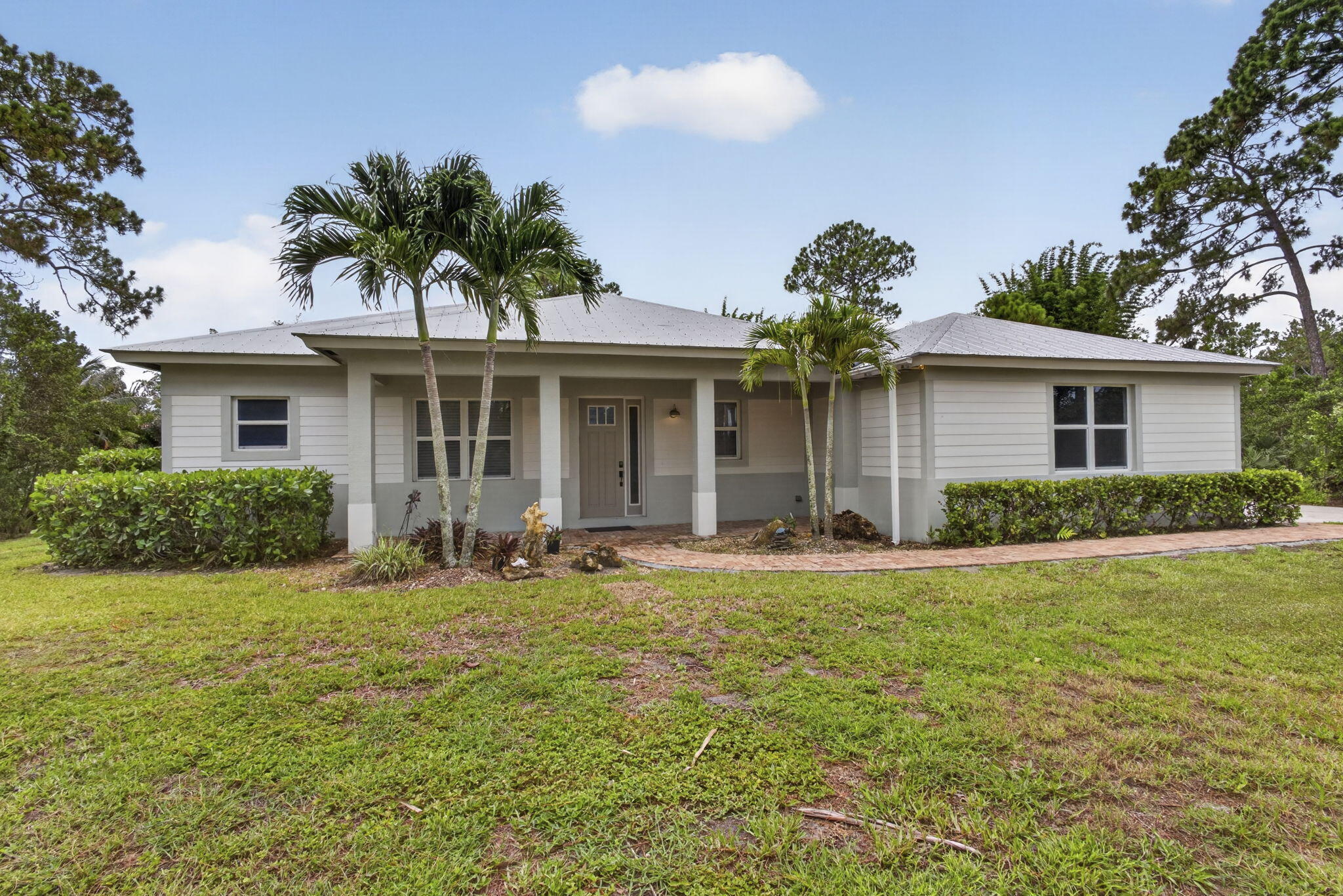 Discover peaceful country living in the highly desirable non-HOA community of The Acreage in Loxahatchee. This custom home with a metal roof offers the perfect blend of comfort, space, and functionality.Inside, you'll find an open-concept floor plan with 10-foot ceilings connecting the living, dining, and kitchen areas. The split-bedroom layout features 4 bedrooms, 2 full bathrooms, and a versatile office/den that can easily serve as a fourth bedroom.The kitchen showcases granite countertops, white shaker cabinets, and plenty of workspace for cooking and entertaining. The spacious primary suite includes a walk-in closet and a private bath with quality Moen fixtures.Enjoy the outdoors from the screened patio overlooking a peaceful pond and fully fenced yard.  The property also features a 12x24 storage shed, carport, custom brick fire pit, and a two-car garage, offering plenty of space for vehicles, storage, and outdoor living.Additional upgrades include impact-resistant windows and doors, a dedicated well-fed irrigation system, and a laundry room with a utility sink and extra storage. Conveniently located near shopping, restaurants, and everyday conveniences, this exceptional home offers the perfect balance of privacy, functionality, and the Florida lifestyle. Schedule your private tour today!