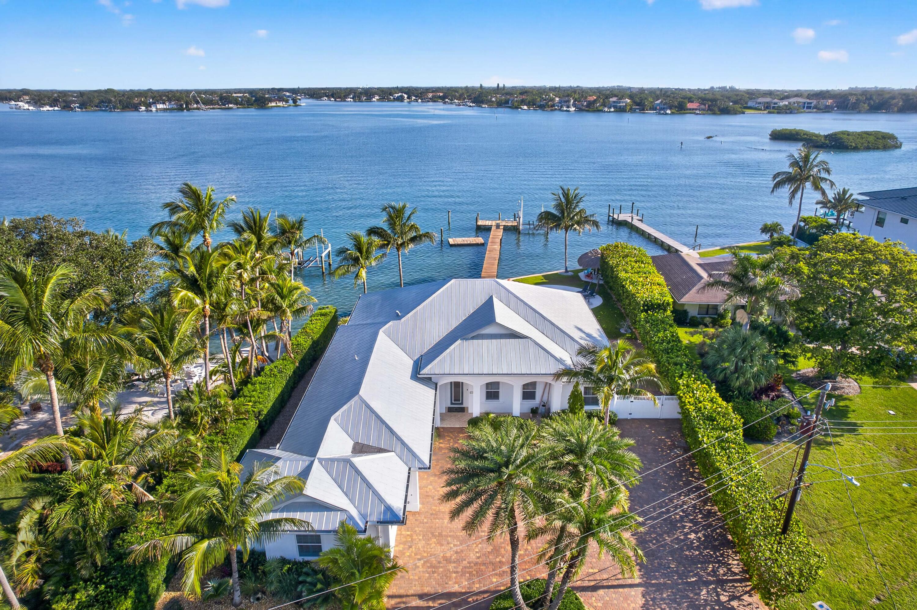 Directly on the wide turquoise blue water of Loxahatchee, this exceptional 2015-built CBS single-story waterfront residence offers the ultimate South Florida boating lifestyle. Situated on an oversized 1/3-acre lot with 110 feet of deep-water river frontage and stunning Bahama-blue water views, this property provides direct access to the Jupiter Inlet and Atlantic Ocean within minutes—making it a true paradise for boaters, fishermen, and waterfront enthusiasts alike.   Designed for both comfortable living and effortless entertaining, the home features approximately 3,000 square feet of air-conditioned living space and over 4,300 square feet total, with 3 bedrooms, 3 bathrooms, and an abundance of natural light throughout the spacious open floor plan. A separate air-conditioned private room adjacent to the garage offers flexibility as VIP guest suite, office, gym, or bonus space.  Interior finishes showcase elegant marble flooring, soaring volume ceilings, crown molding, plantation shutters, and fine custom craftsmanship throughout. The gourmet chef's kitchen flows effortlessly into the expansive living and dining areas and is beautifully appointed with an oversized granite island, custom cabinetry, and premium appliances including a professional-grade gas range—creating the perfect setting for everyday living and entertaining alike.  The luxurious primary suite offers stunning water views and a spa-inspired bathroom complete with dual vanities, a frameless glass shower, soaking tub, and custom walk-in closets.  Step outside to your private tropical oasis featuring a resort-style pool and spa, expansive covered outdoor living areas, lush, private landscaping, and a fully equipped summer kitchen with BBQ grill and refrigerator. The 100-foot private dock includes a seating area and boat lift, offering ample space for multiple watercraft and endless days enjoying the blue-water lifestyle.  Swim, fish, or paddleboard directly from your backyard while watching boats cruise by on the river. Rarely does an opportunity like this become available in such a desirable "in-town" waterfront location. The property also offers a voluntary HOA of only $100 annually, which includes access to a private neighborhood boat ramp.