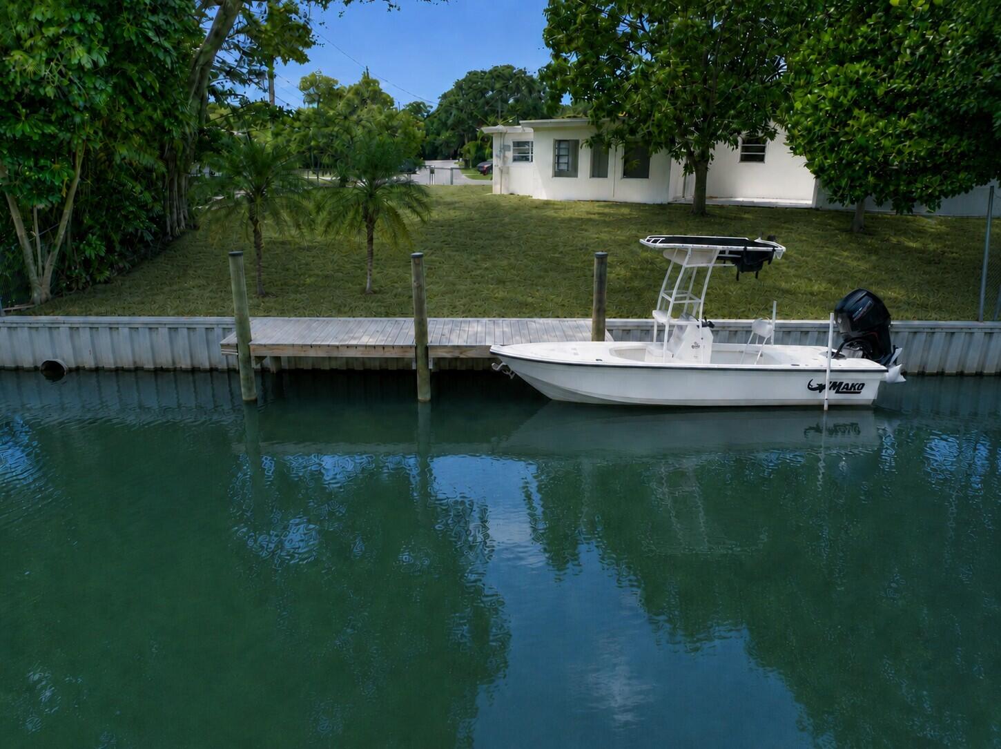 A rare waterfront property set on a premium corner lot, featuring a new boat dock, on one of the most sought-after streets in Lake Clarke Shores. Ideally situated on a quiet canal just one home from the widest section of Lake Clark. Unlike typical waterfront homes, this home's water views are not into neighboring backyards, but instead enjoy a more tranquil, tropical view. Close enough to the wide lake for exciting boating, waterskiing and jet skiing yet set back just enough to enjoy quieter, calmer waters. The property features a new boat dock with composite deck (constructed in 2025) and a seawall spanning the length of the generous corner lot backyard.  From the backyard dock, enjoy direct access to an extensive freshwater boating network connecting Lake Clarke to Lake Osborne and Lake Ida—perfect for exploring miles of scenic waterways. The home offers over 2,200 total square feet with a versatile floor plan, including 4 bedrooms and 3 full bathrooms, plus a living room and family room. Two primary bedroom suites are thoughtfully positioned apart from the additional bedrooms. One suite features a private exterior entrance—ideal for an in-law suite, guest quarters, or potential rental opportunity. A second bedroom also includes its own exterior access, offering additional flexibility. The family room showcases large windows with tranquil canal views and a sliding glass door leading to a concrete patio. The good-sized kitchen overlooks the backyard and water, providing a functional layout with great potential. Additional highlights include a large circular driveway with ample parking and a covered carport that leads into the laundry room and kitchen. Enjoy waterfront living with a private dock, tranquil canal views, and stunning sunsets — ideal for recreation, relaxing and entertaining. Lake Clarke Shores is a highly-regarded, non-HOA community offering its own police department, a boat ramp, tennis and pickleball courts, playground, and conveniently located very close to ocean beaches, downtown West Palm Beach, Palm Beach Island, PBIA airport, I-95, dining, and more. Buyer to verify measurements and information. Sold As-Is, cash offers only. LWDD Canal and right-of-way. Seller is a licensed sales agent.  Some photos virtually staged.