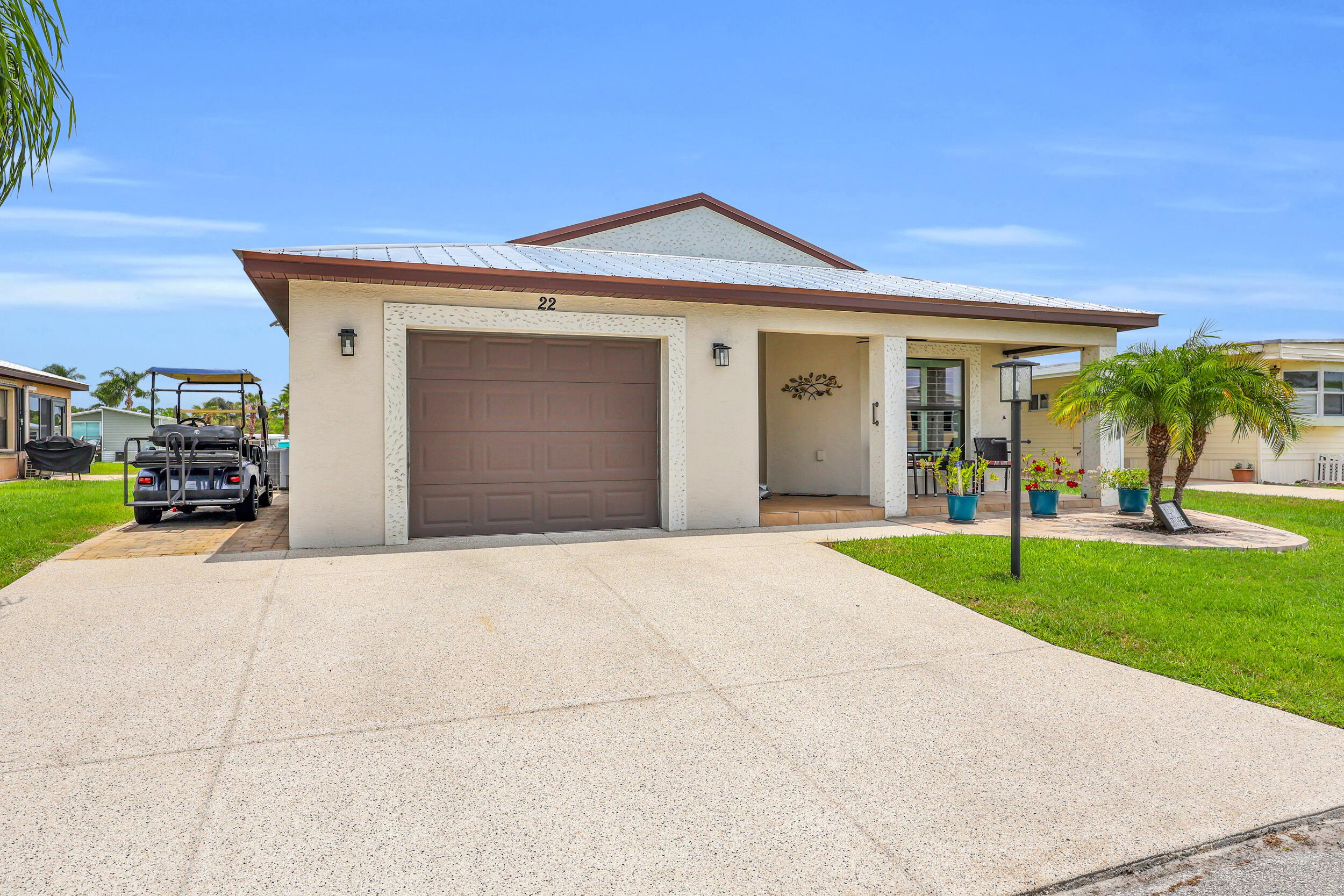 Welcome to 22 Alta Loma in the sought-after Spanish Lakes One community, a vibrant 55+ waterfront neighborhood offering an active Florida lifestyle with amenities included in the monthly lot rent.     Built in 2018, this CBS construction home features a metal roof, impact windows and doors throughout, and has been meticulously maintained. From the moment you arrive, you'll appreciate the covered front porch and attractive curb appeal.     Inside, the open-concept floor plan offers 2 beds, 2 baths, vaulted ceilings, a spacious living, dining, and kitchen area designed for comfortable everyday living and entertaining.    The kitchen is a standout feature with white cabinetry (rare find in the community) granite countertops and backsplash, stainless steel appliances, and built-in pantry.    The primary living areas feature tile flooring, while the bedrooms offer the comfort of carpeting. Plantation shutters, upgraded lighting, and ceiling fans throughout add both style and functionality.     The split-bedroom floor plan provides privacy for owners and guests, while the interior laundry room includes a washer and dryer for added convenience.     One of the home's most enjoyable features is the enclosed lakeside patio, complete with impact windows and its own mini-split air conditioning system, creating the perfect year-round space to relax and enjoy the water views. Outside, an additional paver patio provides a convenient area for golf cart parking, storage, and easy maintenance.     The monthly land lease includes lawn care, irrigation, trash removal, and access to an impressive array of amenities designed to keep you as active and social as you'd like to be.  Enjoy two heated swimming pools, a clubhouse with kitchen and lounge, auditorium with stage, library, arts and crafts room, billiards hall, fitness center, sauna, woodworking shop, card room, tennis courts, pickleball courts, bocce, shuffleboard, horseshoes, softball field, and even a Par-3 nine-hole golf course. Whether you're looking to stay active, pursue hobbies, or meet new friends, there's always something to do just steps from your front door.