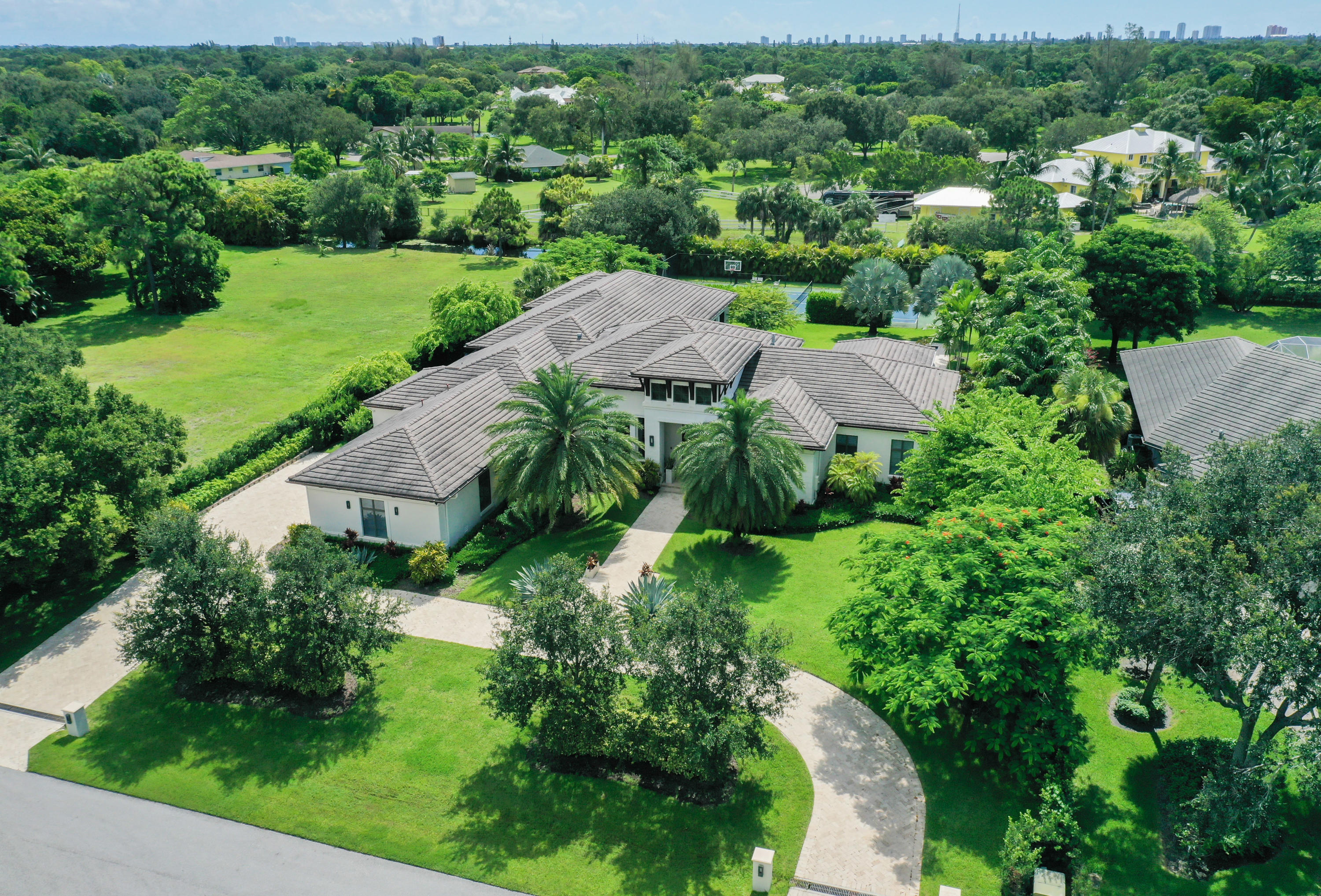 Custom Steeplechase estate featuring superb quality throughout, this home truly checks all the boxes and then some. Situated on over one acre, the home boasts over 6,800 square feet under air, all on one level, allowing you to take full advantage of indoor and outdoor Florida living.The home has five well-appointed bedrooms, each with luxurious bathrooms and spacious custom fitted walk-in closets. The grand owner's suite, separate from the other bedrooms, features opulent his and hers bathrooms (his features a steam shower) and room size custom fitted closets. The gourmet kitchen, family room and sunny breakfast area center the house. The thoughtfully designed kitchen features a Dornbracht sink and hardware, Calcutta gold marble slabs, Sub Zero refrigerator and freezer, two Miele dishwashers, Wolf appliances, including a full steam oven and Miele coffee/espresso machine. Steps from the kitchen are a butler's pantry with sink and two refrigerator drawers and a wine room complete with wine refrigerator. Rounding out the indoor space is a sophisticated home office, formal dining room, living room with a large fireplace, mirrored gym, large playroom/clubroom and custom home theater.
Floor to ceiling glass pocket doors open to extend the living space off of the family room into the nearly 1,000 sq ft covered loggia complete with summer kitchen hosting a 36" Wolf BBQ and phantom retractable screens. The backyard is enveloped by mature landscaping and lush greenery for maximum privacy. Beautiful pool and spa with an electric pool cover, tennis court and plenty of open yard area for other recreation. Some additional home features include solid walnut flooring throughout, custom window treatments in all rooms and bathrooms, impact windows, full house generator, security system with indoor and outdoor cameras, and built- in speakers throughout. The 3-car garage is fully tiled and air-conditioned. There are truly too many features to list. This residence is perfect for the most discerning buyer looking for the ultimate in luxury, privacy, and comfort. This exceptional estate offers every modern convenience. This is a true gem in the heart of Steeplechase.