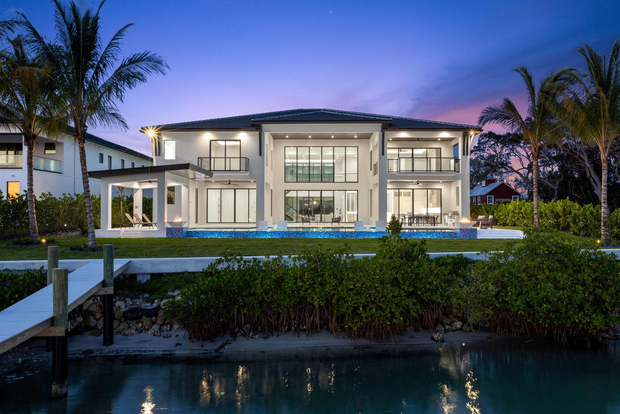 Discover this stunning waterfront masterpiece of exceptional new construction on the scenic Loxahatchee River, offering breathtaking blue water views and unparalleled luxury. Grand interiors feature 23-foot ceilings, a spectacular floating staircase, and an expansive family room, ideal for entertaining. A gourmet, chef's kitchen boasts backlit quartz countertops and seamless water views. Encompassing over 2,000 square feet, a luxurious master suite incorporates a breakfast bar, sitting room with a fireplace, two oversized closets, a spa-like bathroom, and a private balcony. Four additional bedrooms have en-suite baths, for a total of 5 bedrooms, 6 full baths, and 2 half baths. An 8-car garage with a car enthusiast's clubroom allows you to keep an eye on your prized vehicles while a den and tackle room round out the living and entertainment areas in this spacious home. Enjoy an outdoor oasis with a two-story covered patio, sunken firepit, infinity-edge pool with fire bowls, oversized hot tub, waterfall-fed pergola, and a new dock with direct water access. This extraordinary home is a boater's dream and the epitome of modern luxury. Don't miss this rare opportunity!