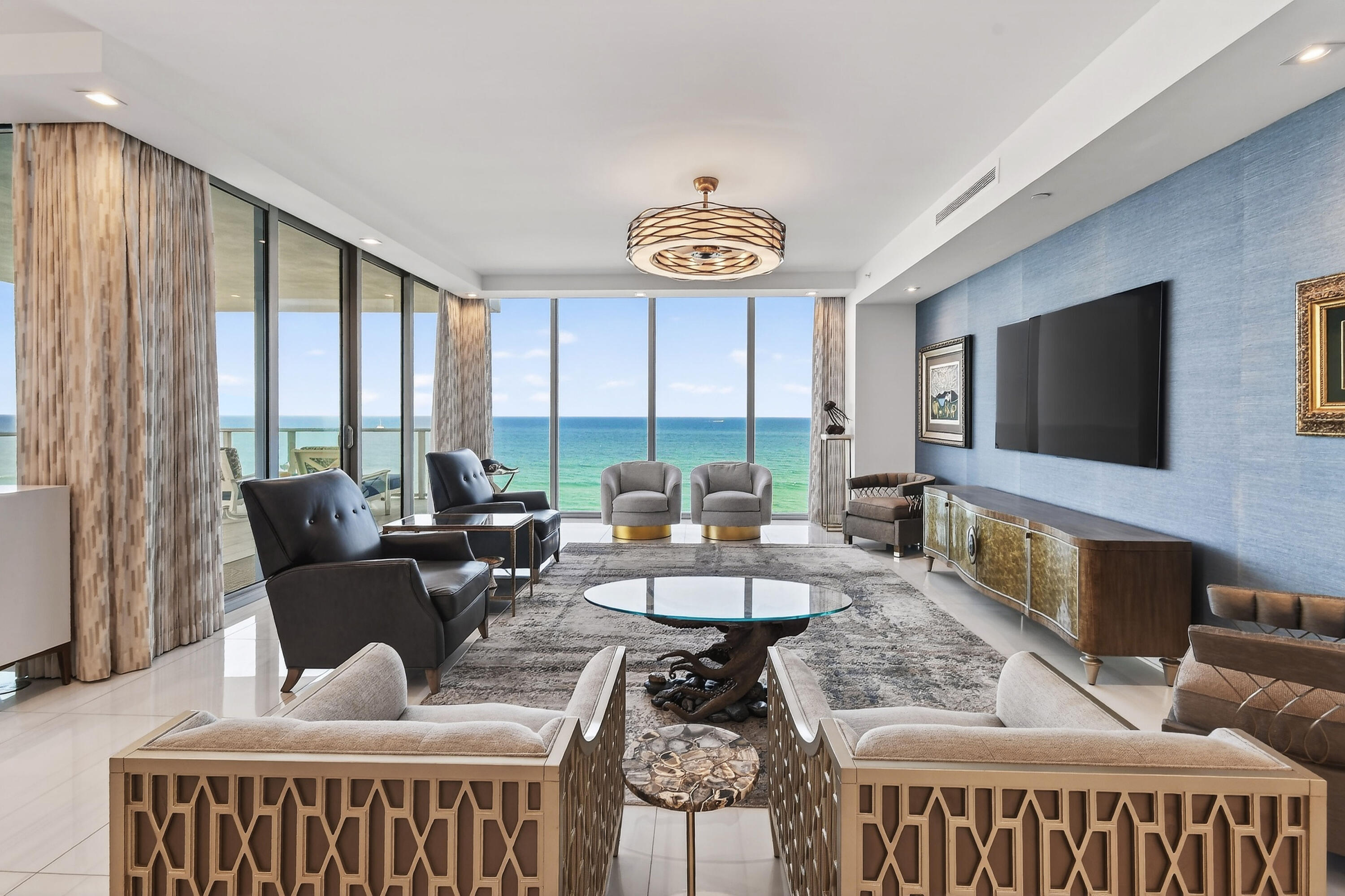 Rising above more than 340 feet of pristine private beachfront, Residence 1001 at 5000 North Ocean is a fully customized oceanfront residence where architectural scale, refined craftsmanship, and panoramic water views converge. This coveted Seabreeze-model residence commands sweeping Atlantic Ocean and Intracoastal vistas through expansive walls of floor-to-ceiling glass, with generous balconies designed for true indoor-outdoor living. Arrival is via a private elevator foyer, offering privacy and scale more commonly associated with a single-family estate than a condominium.  The interior has been extensively upgraded, well beyond original specifications. Large-format polished porcelain flooring flows throughout the home, complemented by custom wood trim and tailored detailing that adds warmth and structure to the contemporary design. The residence balances clean modern lines with carefully executed architectural craftsmanship.  The kitchen serves as both a visual centerpiece and a functional workspace, featuring an Azul Macaubus quartzite social island with dramatic waterfall edges, white quartzite countertops and a full-height coordinating tumbled glass backsplash. A complete Thermador appliance suite, integrated lighting, upgraded fixtures, and the generously proportioned social island support both daily living and entertaining. Upgraded cabinetry and refined finishes maintain a seamless connection to the adjoining living areas.  Entertaining spaces are thoughtfully designed and highly customized. The elegant great room opens to the spacious wrap-around balcony, offering breath-taking views of both the ocean and intracoastal waterway. The game/media room features an exquisite custom wet bar with waterfall edge finished in a stunning semi-precious stone that complements the custom cabinetry with display storage; paired refrigeration; stainless steel accents; and integrated lighting. The wet bar countertop was selected with intent to coordinate with the kitchen island to enhance design cohesion.  Lighting throughout the residence has been intentionally curated, incorporating sculptural chandeliers, designer pendants, recessed architectural lighting, and upgraded ceiling fixtures that define each space with clarity and balance.   The primary suite offers balcony access and expansive ocean and intracoastal views. It includes custom-designed closet systems and a refined spa-style bath appointed with large-format porcelain wall and floor tile, floating dual vanities with integrated storage and stone countertops selected for durability and visual continuity. A freestanding soaking tub serves as a sculptural focal point, while the glass-enclosed shower features bench seating, recessed niches, and upgraded fixtures designed for both comfort and performance. Backlit mirrors, full-height custom glass wall tile, tailored cabinetry, and curated hardware selections complete the space, creating a bath that feels architectural, calm, and deliberately understated.  Guest bedrooms and secondary living spaces continue the same level of finish, with custom trim detailing, integrated lighting, motorized window treatments, and cohesive material selections throughout. A well-appointed powder room features designer wall coverings, modern fixtures, and custom cabinetry. Additional enhancements include sun-protection film on all exposures, electrical and lighting upgrades, custom closet interiors, and discreet entry detailing for improved sound and light control.  Designed by Randall Stofft Architects, 5000 North Ocean is a 19-story oceanfront landmark set across 4.5 acres of preserved dunes and natural habitat. Residents enjoy a private beach sanctuary, oceanfront pool, state-of-the-art fitness center overlooking the Atlantic, resident club room, concierge services, valet parking, and a 24-hour attended security.  Located just minutes from Palm Beach International airport, Worth Avenue, championship golf, tennis, and world-class dining, Residence 1001 presents a rare opportunity to acquire a fully customized, move-in-ready oceanfront home within Singer Island's newest and most exclusive address.