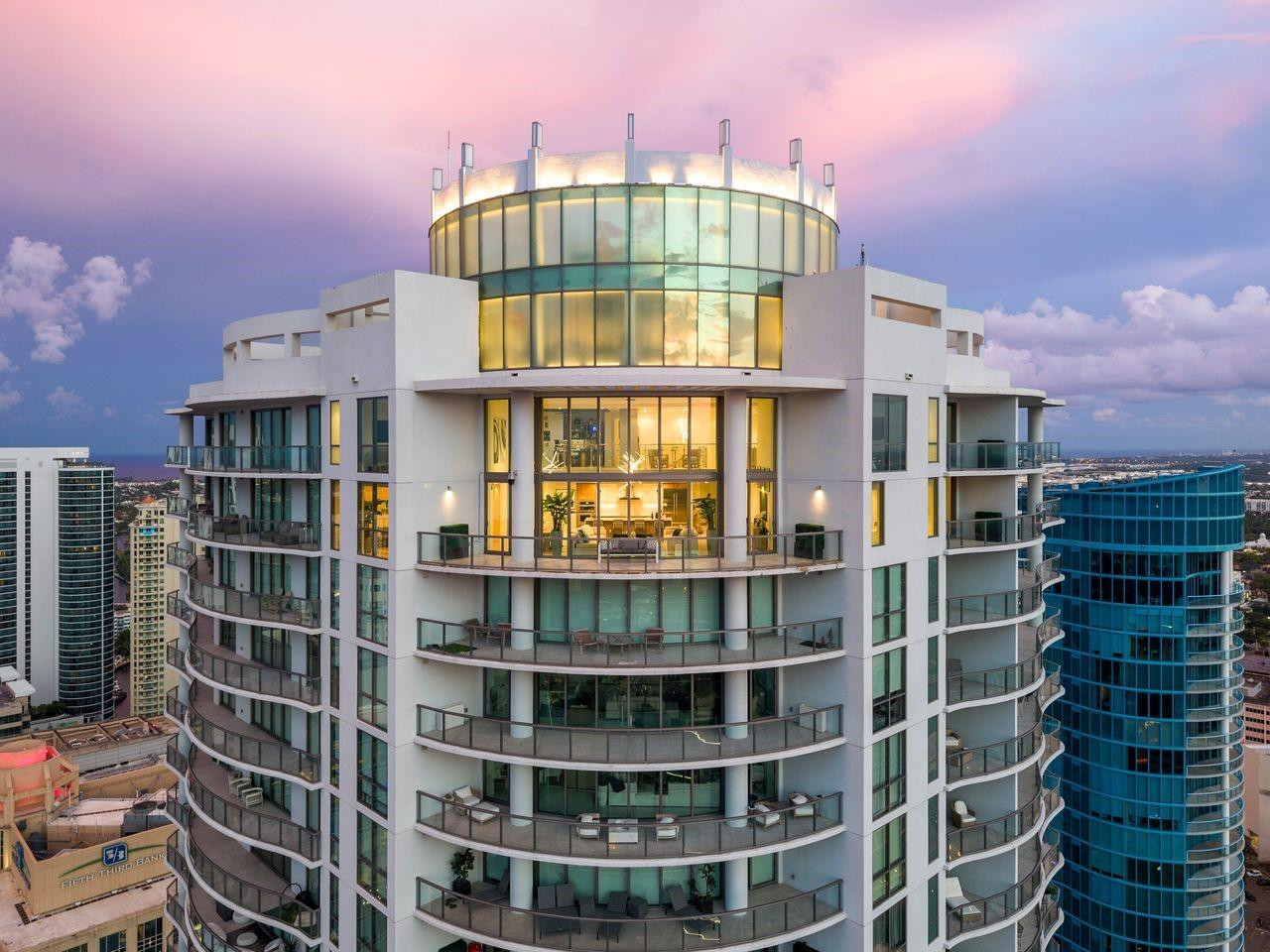 Soaring above Downtown Fort Lauderdale, 100 Las Olas is the city’s most coveted address. This one-of-a-kind, two-story penthouse—the city’s highest—offers 5,281 sq. ft. with 5 bedrooms, 6.5 baths, and 4 parking spaces. Dramatic 20–30 ft. ceilings, walls of glass frame panoramic skyline views, while a fully integrated Magnolia sound system, custom-designed televisions, professional-grade camera security, and a commercial internet network create a sophisticated smart-home environment. The open great room flows to a curved terrace for extraordinary indoor-outdoor living. With top-tier appliances, designer finishes, and world-class amenities steps from premier dining and shopping, this residence defines modern luxury. Soaring above Downtown Fort Lauderdale, 100 Las Olas is the city’s most coveted address. This one-of-a-kind, two-story penthouse—the city’s highest—offers 5,281 sq. ft. with 5 bedrooms, 6.5 baths, and 4 parking spaces. Dramatic 20–30 ft. ceilings, walls of glass flood the home with natural light while framing panoramic skyline views. A built-in sound system and integrated camera security add modern convenience. The open great room flows to a curved terrace for extraordinary indoor-outdoor living. Featuring top-of-the-line appliances, designer finishes, and access to world-class amenities, all just steps from premier dining, shopping, and entertainment.