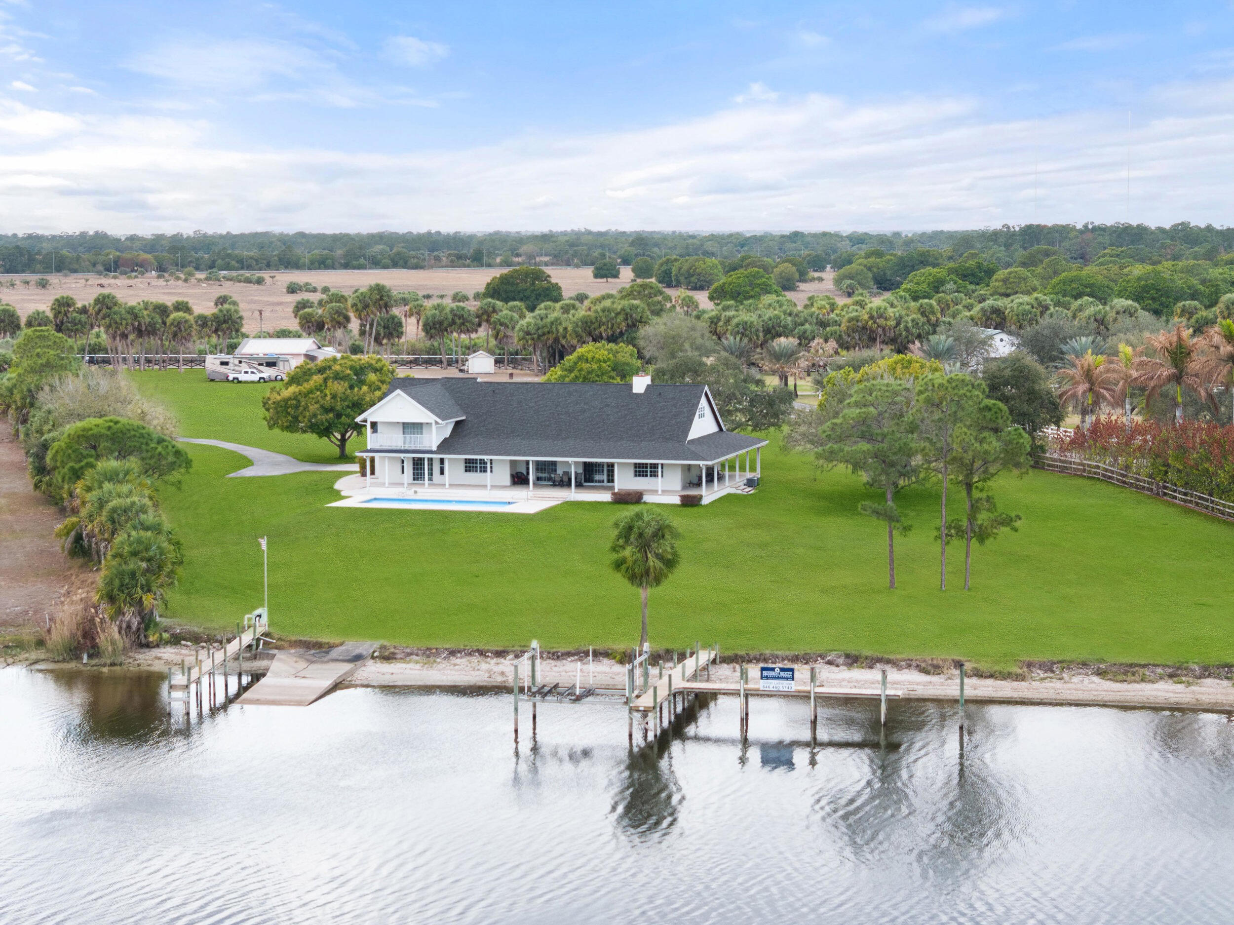 5 ACRES!! 380 SF OF WATER FRONT!! From sunrise until sunset, you will feel like you're on vacation every day at this rare 5 acre private waterfront estate in Palm City. Agricultural and Equestrian use allowed. Unmatched Serenity and peace abound as you overlook the water from the wrap around porch or the upstairs balcony. Sitting at roughly 30 feet of elevation, the views are stunning.  The home features 4785 square feet of living space which includes attached guest quarters, making it perfect for entertaining or multigenerational families. Boasting 5 bedrooms all with en-suite baths, 2 kitchens and multiple flex rooms the home awaits your personal touch to fulfill your vision and make it your own.  Outside you will find 5 cleared acres of natural beauty for outside activities or adding ....additional living quarters. There is a 2000 square foot workshop with enough additional space to store your water toys or extra vehicles. Overlooking the river is an 18' by 40' private pool, 2 boat docks and a boat ramp permitted by USACE and over 380' of water frontage. Natural beach shoreline with minimal erosion. Situated on the St. Lucie River which connects the Atlantic to the Gulf of Mexico it is a boater's paradise, allowing easy navigation from the east coast to the west coast with deep water and no fixed bridges.   The property is also just minutes from the newly developed Apogee Golf Club, one of South Florida's most exclusive private golf destinations featuring multiple championship courses and world-class amenities.  Major capital improvements completed in April of 2024, include a new roof, new gutters and downspouts and exterior paint. The well pump and 2 AC units were replaced in 2021.  Whether you choose to enjoy the property as-is, expand, or re-imagine it entirely, opportunities of this size, frontage, and permitting are extraordinarily rare.