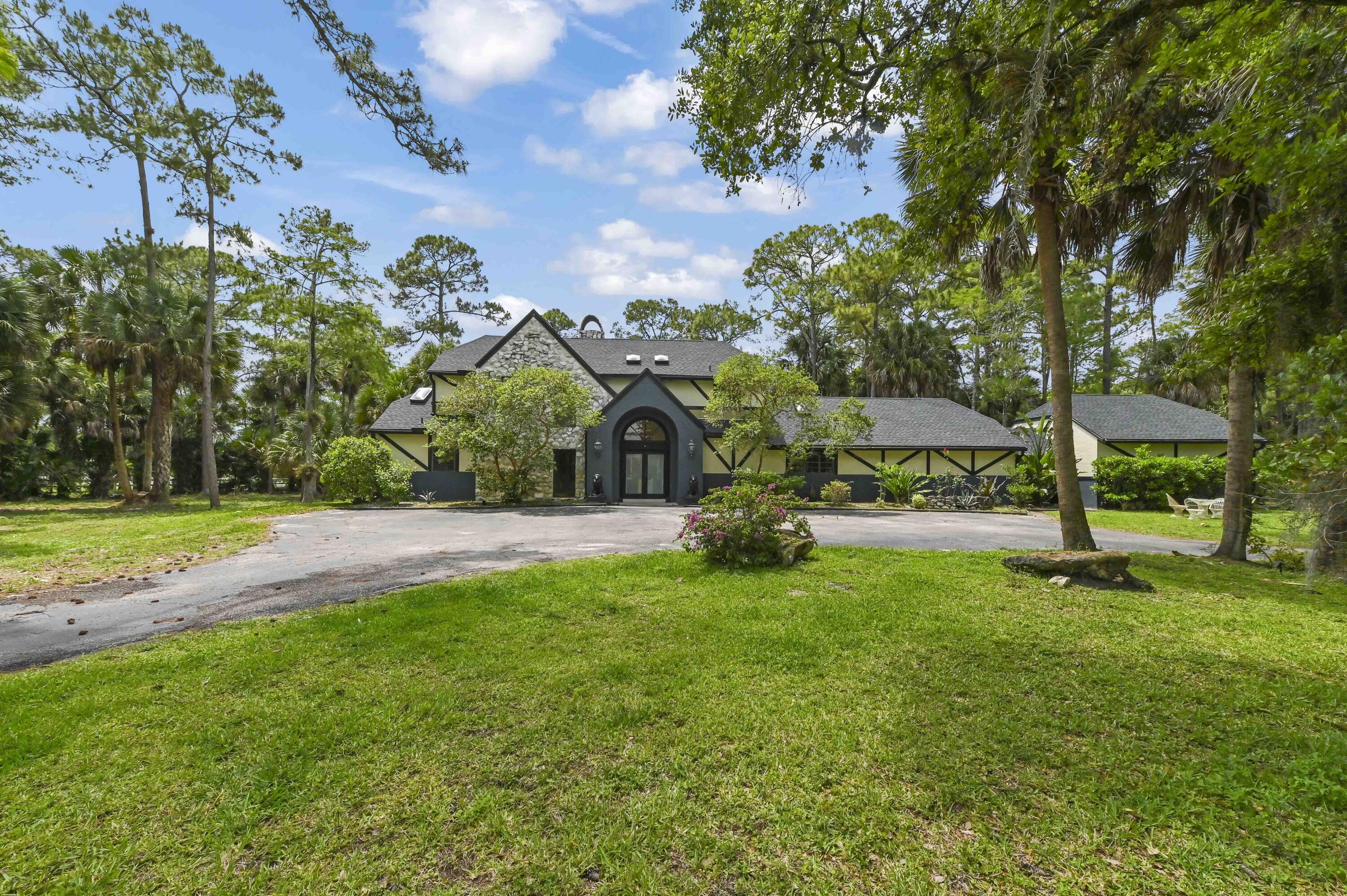 Privacy, space, and a long list of recent upgrades — this is the Fox Trail estate buyers have been waiting for.  Set on 5 gated acres in one of Palm Beach County's most desirable communities, this distinctive Tudor-style estate delivers the space and freedom that's nearly impossible to find at this price point. With a 2024 roof, 2020 AC, 2025 pool and garage updates, 2023 bathrooms, updated flooring, and a 2026 whole-home carbon filtration system, the heavy lifting is done — this is truly a move-in ready property.  The main residence offers 3 bedrooms and 3 full ensuite bathrooms plus a half bath, with soaring ceilings, a wood-burning fireplace, and generous living spaces across two stories.  The kitchen is built for entertaining — granite countertops, center island, bar seating, cooktop, and full appliance package, with a convenient laundry room tucked nearby.  The detached guest house is a rare feature at this price: a fully self-contained 1 bedroom, 1 bathroom retreat with its own full kitchen, living area, and private balcony. Whether you're housing family, a property caretaker, or simply want the option of rental income, this space adds tremendous flexibility and value.  Step outside to your own private resort — a screened in-ground pool, covered deck, a full detached cabana bathroom, and lush landscaping on 5 open acres. A grand circular driveway makes a statement on arrival and offers parking for cars, trailers, and guests alike.  For those who want the option of a horse or two without the commitment of a professional facility, the property includes a 3-stall barn and tack room, with ample space to add paddocks or a private arena — perfect for hobby equestrians, weekend farm life, or simply extra storage. And as a resident of Fox Trail, you'll have access to 29 miles of private riding trails right outside your gate.  This is not a compromise — it's a lifestyle. Space, upgrades, a guest house, a pool, and 5 private acres in a gated equestrian community, all for under $1.5M in Palm Beach County.