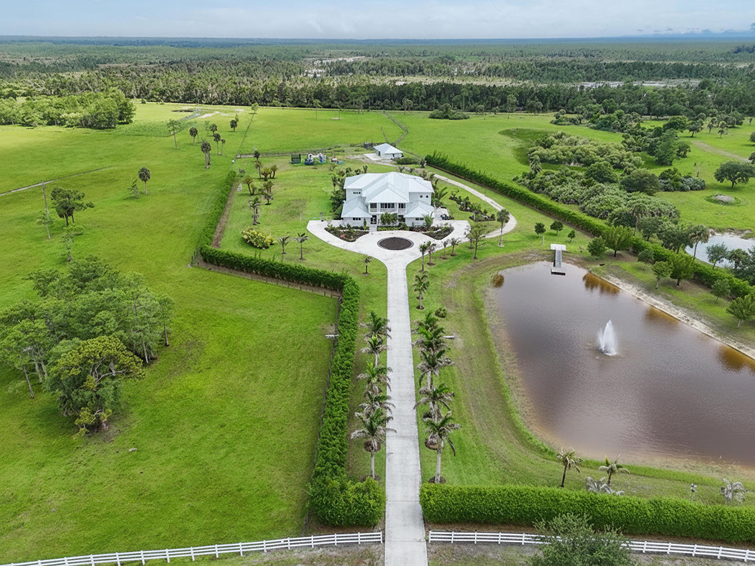 Tucked behind the gates of an exclusive equestrian community, this extraordinary custom estate offers a rare blend of luxury, privacy, and acreage. Built in 2020 and set on 35 fully fenced acres, the property features over 7,500 square feet of living space with 7 bedrooms, 7.5 baths, impact glass, an elevator, and exceptional craftsmanship throughout. Designed for both everyday living and grand-scale entertaining, the home showcases a chef's island kitchen, expansive living areas, formal dining room, game room, and private den/safe room. The luxurious primary suite offers a gas fireplace and tranquil views across the estate. Outside, a resort-inspired setting awaits with a spectacular tiki pavilion, summer kitchen, heated pool and spa, four screened porches, and beautifully landscaped  grounds complete with extensive lighting, a pond, fountain, and private dock. A substantial CBS utility building provides exceptional storage and workshop space, while the split four-plus-car garage, whole-house generator, and prime location near Stuart, Jupiter, shopping, and major highways complete this remarkable offering. A private retreat where luxury, land, and lifestyle come together on an impressive scale.