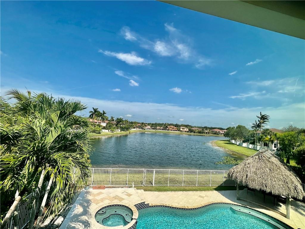 Welcome to the "Picasso" of Isles at Weston," a stunning lakefront home showcasing exceptional upgrades and thoughtful design throughout. A dramatic waterfall entry, soaring ceilings, marble flooring, designer chandeliers, custom crown molding, and breathtaking sunset views create an unforgettable living experience. The first-floor primary suite offers privacy and convenience, along with a powder room for guests. Enjoy a custom 4K projector home theater with 7.1 surround sound, expanded gourmet kitchen, updated bathrooms, impact windows/doors, EV charger outlet, and smart irrigation system. Relax in the oversized pool/spa with new Diamond Brite, tiki hut waterfall, outdoor kitchen, and expansive pool deck overlooking the lake. Low HOA $341/month includes 400MB fiber internet, expanded cabl
