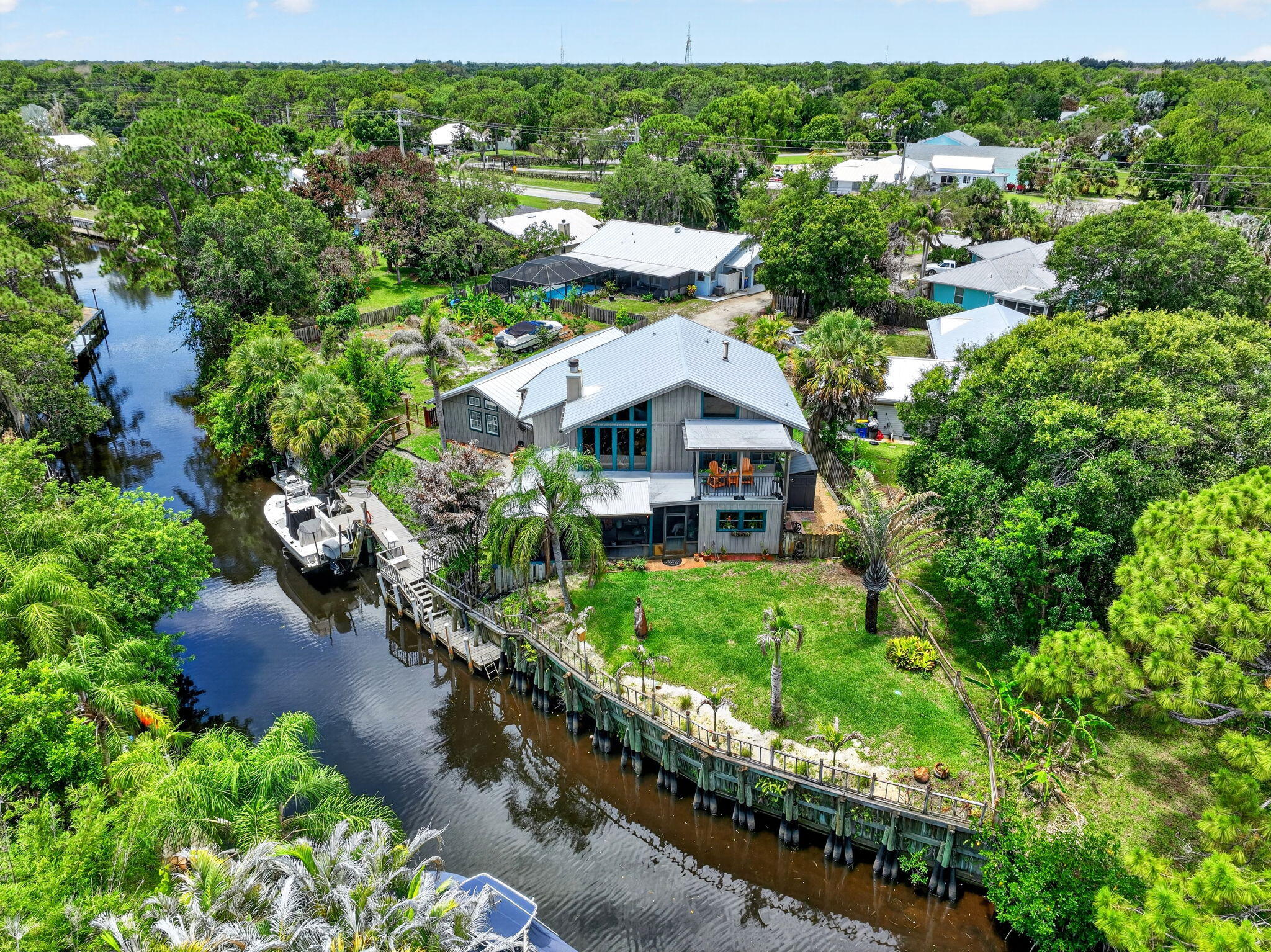 Rare Palm City waterfront retreat with no fixed bridges and direct ocean access. This distinctive 5BR/3BA home offers approx. 2,534 living sq ft with warm wood detailing, soaring ceilings, dramatic fireplace, and flexible living spaces full of character. The layout includes a downstairs primary suite plus an upstairs suite currently used as an art studio. Enjoy boating from your private dock with lift and electric, seawall and dock in good condition. Additional highlights include a 2023 metal roof, complete panel shutters, newer appliances, paver driveway, oversized garage with epoxy floors, low annual HOA for road/canal maintenance, and peaceful waterfront setting. A unique opportunity for buyers seeking boating, privacy, and a home with true personality. The oversized attached garage is approximately 26 feet deep and offers excellent space for vehicles, tools, and recreational storage.  The upstairs master suite is currently used as an art studio and provides flexible options for a guest retreat, home office, media room, creative space, or additional private living area. The floor plan offers separation between the downstairs primary suite and upstairs living space, creating functionality for guests, remote work, or family living.  The private dock, lift, electric service, and well-maintained seawall support the Palm City waterfront lifestyle. Low annual HOA of approximately $244.77 primarily supports road and canal maintenance.