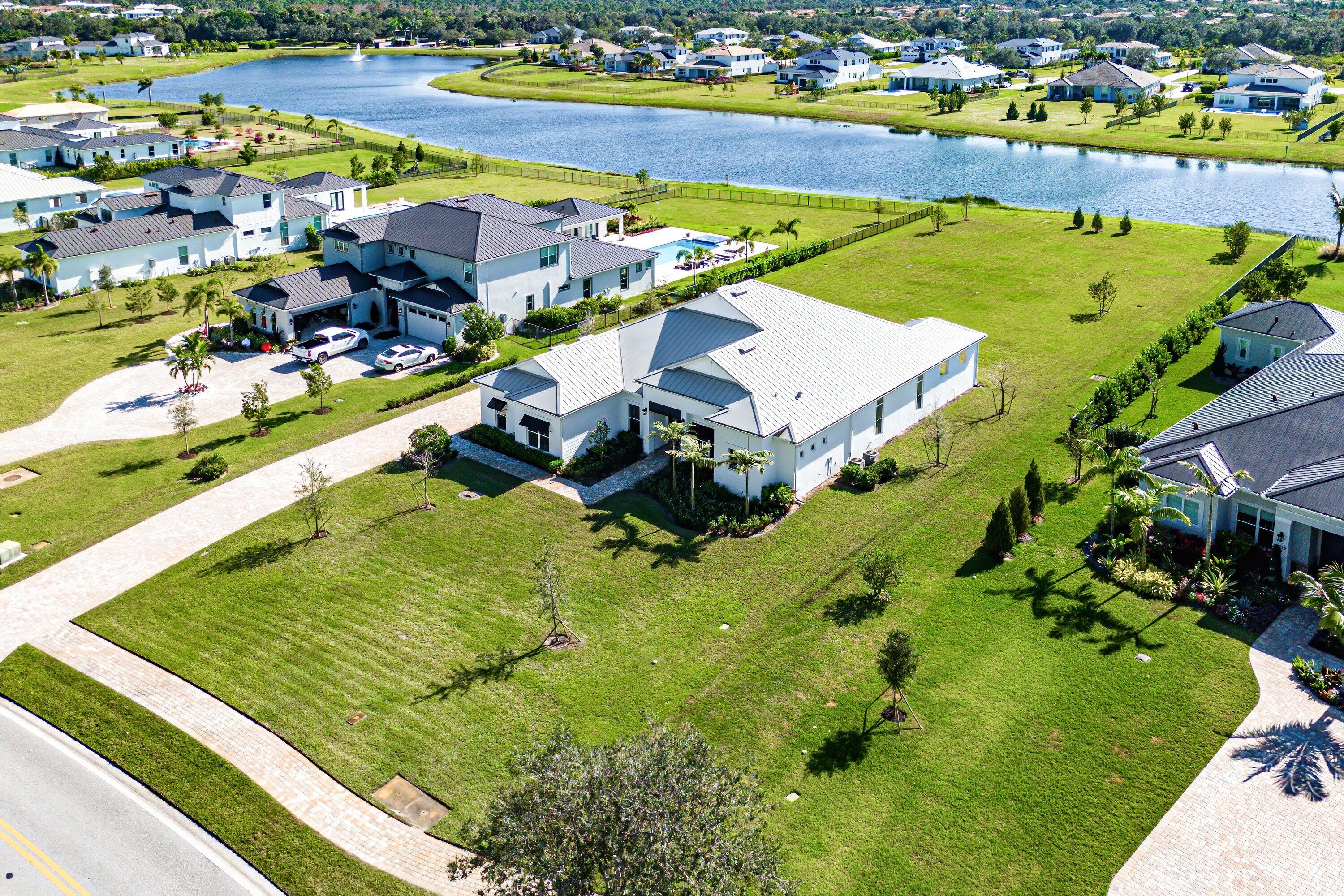 Single story Oakley home with lake views on a just shy 1 acre homesite in an exclusive, high end community. This brand new residence has never been lived in and offers a desirable open concept layout, perfect for both everyday living and entertaining. The home has been professionally staged is offered furnished as seen. A dramatic zero corner sliding door set opens all the way to allow full indoor outdoor living and floods the home with natural light. Beautiful engineered hardwood and tile floors run throughout, complemented by contemporary, high end light fixtures for a sleek, modern feel. The gourmet kitchen is a true showpiece, featuring: " KitchenAid gas cooktop " Three ovens ideal for large family gatherings and entertaining " Soft close drawers and cabinetry " Large walk in pantry With 4 bedrooms, and  a flex room that can function as a 5th bedroom, an office, a study, media room, or playroom and 3 baths, the floor plan is both functional and versatile. Bedrooms 2 and 3 share a convenient Jack and Jill bathroom, while a separate cabana bath provides direct access to the outdoor area perfect for a future pool.  An extended covered patio, pre wired and plumbed for an outdoor kitchen,  enhances the outdoor living experience, offering a generous space for lounging, dining, and entertaining. The expansive just shy of 1 acre lot provides incredible potential to expand your private oasis with a guest house, resort style pool and spa, outdoor kitchen, or even a tennis/pickleball court. Prime location just 5 miles from the beach, surrounded by world class golf, boating, fishing, shopping, and scenic hiking and biking trails. Enjoy easy access to major highways and only about 25 minutes to Palm Beach International Airport (PBIA). A rare opportunity to own a new, never lived in luxury home with room to grow and customize to make this your forever dream home.