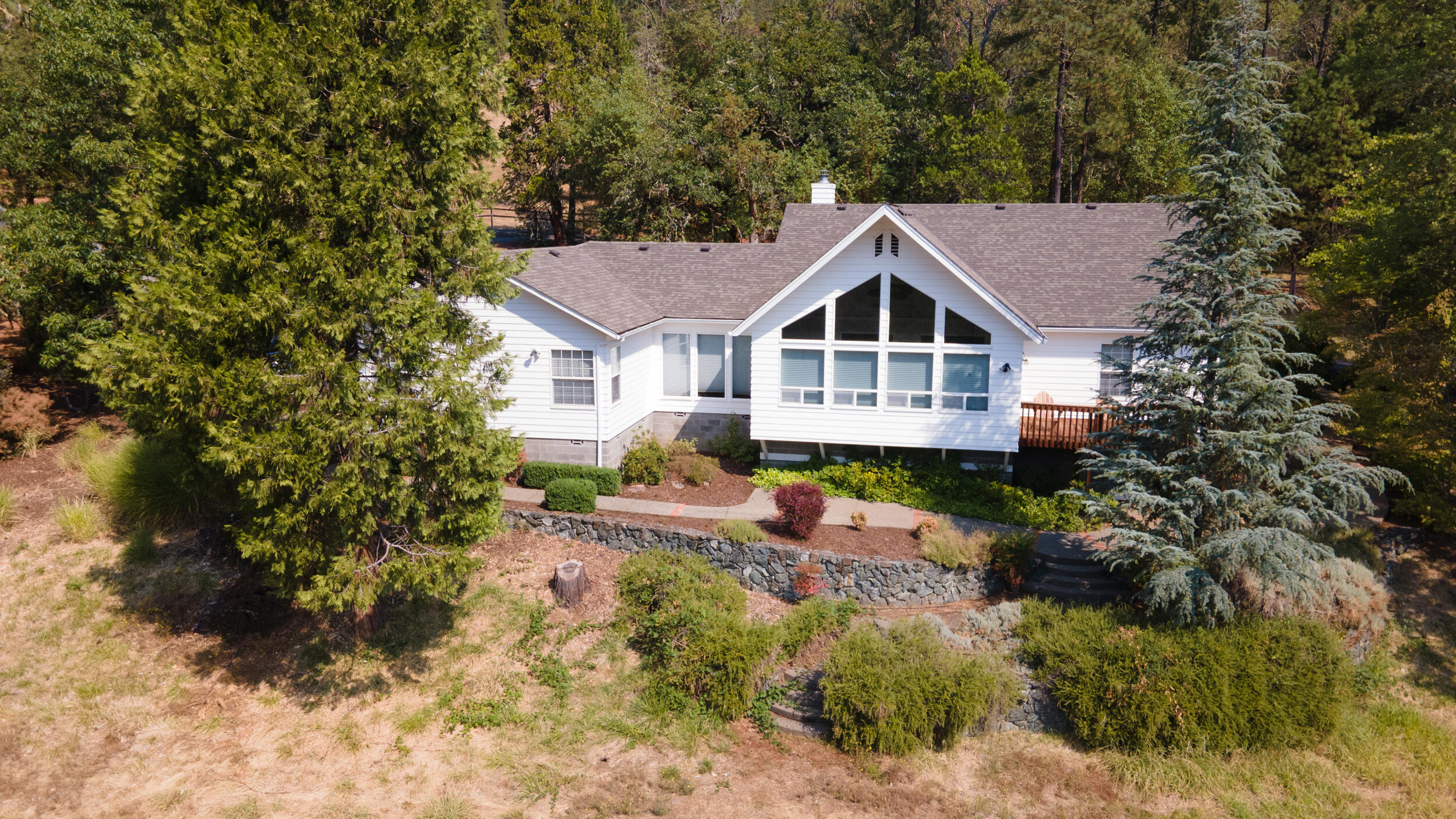 Private, gated, single-level home in the heart of Southern Oregon's lush countryside. Nestled in 8+ acres and just a stroll from Fish Hatchery Park, this lovely 3-bed, 2.5-bath home spans 2,500+sqft. Open-concept layout flows effortlessly from the front door into the kitchen and family room addition, where floor-to-ceiling windows frame panoramic views of surrounding mountains. Landscaping is low-maintenance, w/ drip irrigation & sprinkler system. Recent, extensive fire mitigation work and fire-resistant siding adds peace of mind while a whole-house propane generator preserves comfort and continuity. A detached shop building offers a bonus garage bay & ample storage. Rear gate leads to a large parking area with space for your RV, boat, or trailer. An inner fence surrounds raised garden beds. Built in 1993 and well maintained overall, the kitchen and bathrooms are dated but easy to update to your taste.