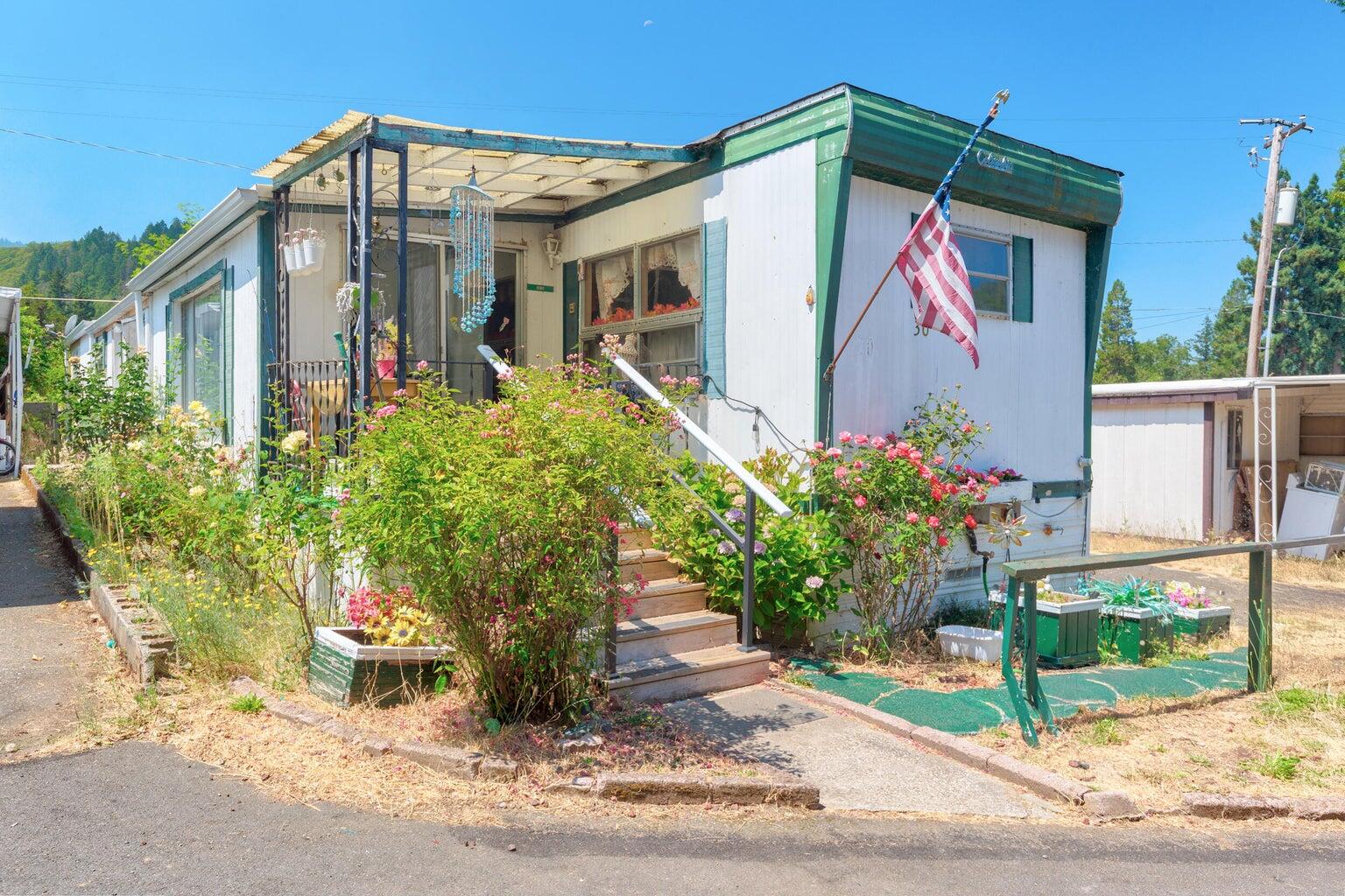 Professionally cleaned and move-in ready. Cozy two bedroom 1 1/2 bath, 1965 mobile located in all ages, pet friendly park. Added on bonus and laundry room not included in the square footage listed for this double wide. Portable A/C, washer (cold water only), dryer, two sheds, and fridge included in sale. Beautiful mountain views with Rogue River right across the road. Conveniently located between Grants Pass and Rogue River.