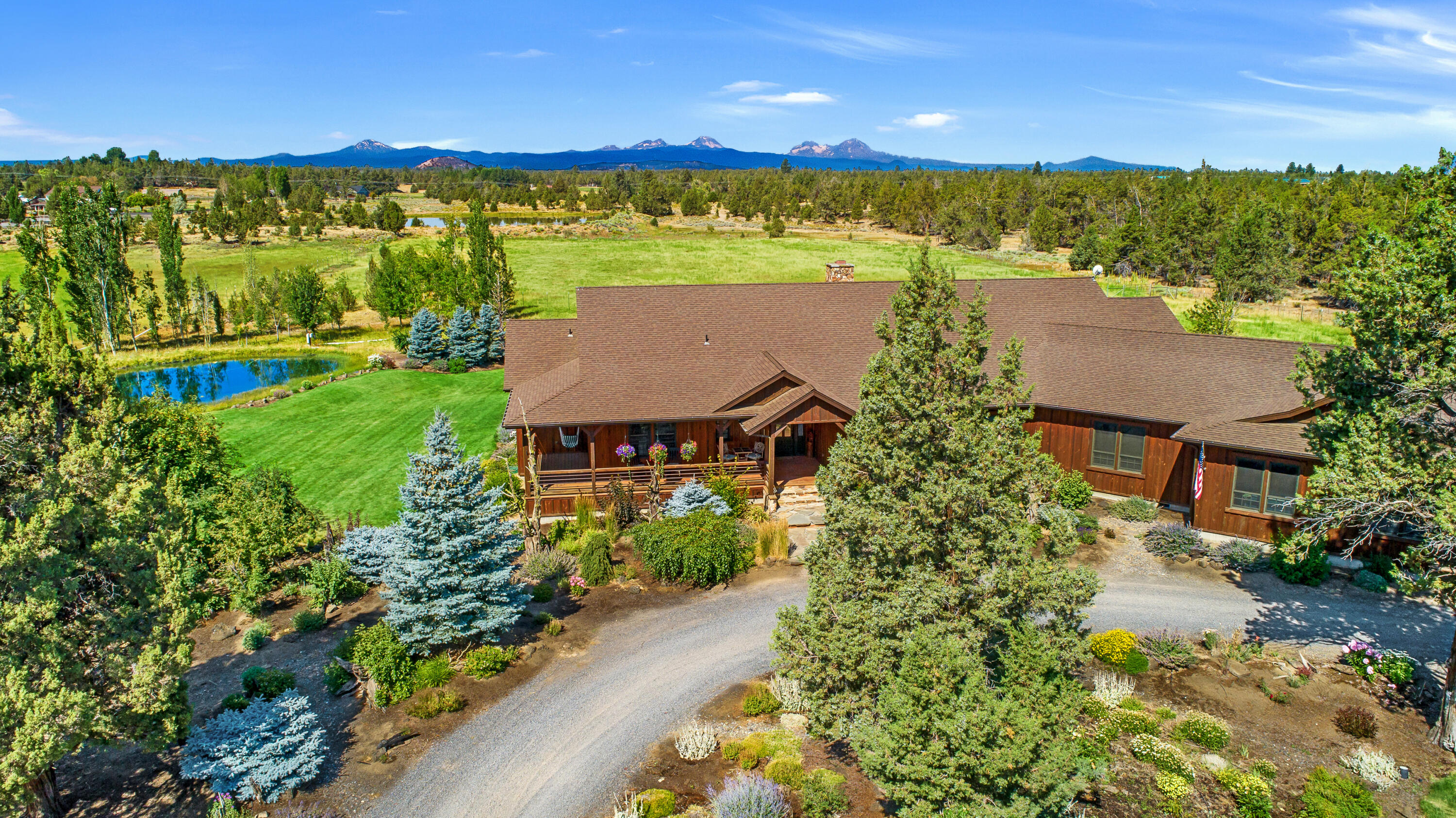 This remarkable 9.75-acre secluded sanctuary boasts breathtaking Cascade Mountain views, over 5 acres of underground automated irrigation, a 36' x 24' shop, & an oversized 3-car garage with 10' doors. Built in 2008, this single-level, 3828sf custom-built home is a true masterpiece, exuding elegance & quality. The main living area features 12' ceilings & 10' ceilings throughout, offering stunning views from Mt Bachelor to North Sister. The kitchen is bright & spacious, with granite countertops. The primary suite is a true oasis, complete with a clawfoot tub, radiant floor heating in the en-suite, & access to the back deck. Two add'l bedrooms, one offering complete privacy for long-term guests with a living area & separate access. The interior is complete with an office, bonus room & spacious mudroom. The exterior features reclaimed wood siding, 1690sf of covered porches, a deck overlooking the pond, a stunning waterfall feature framed by the mountains, an orchard, & a greenhouse.